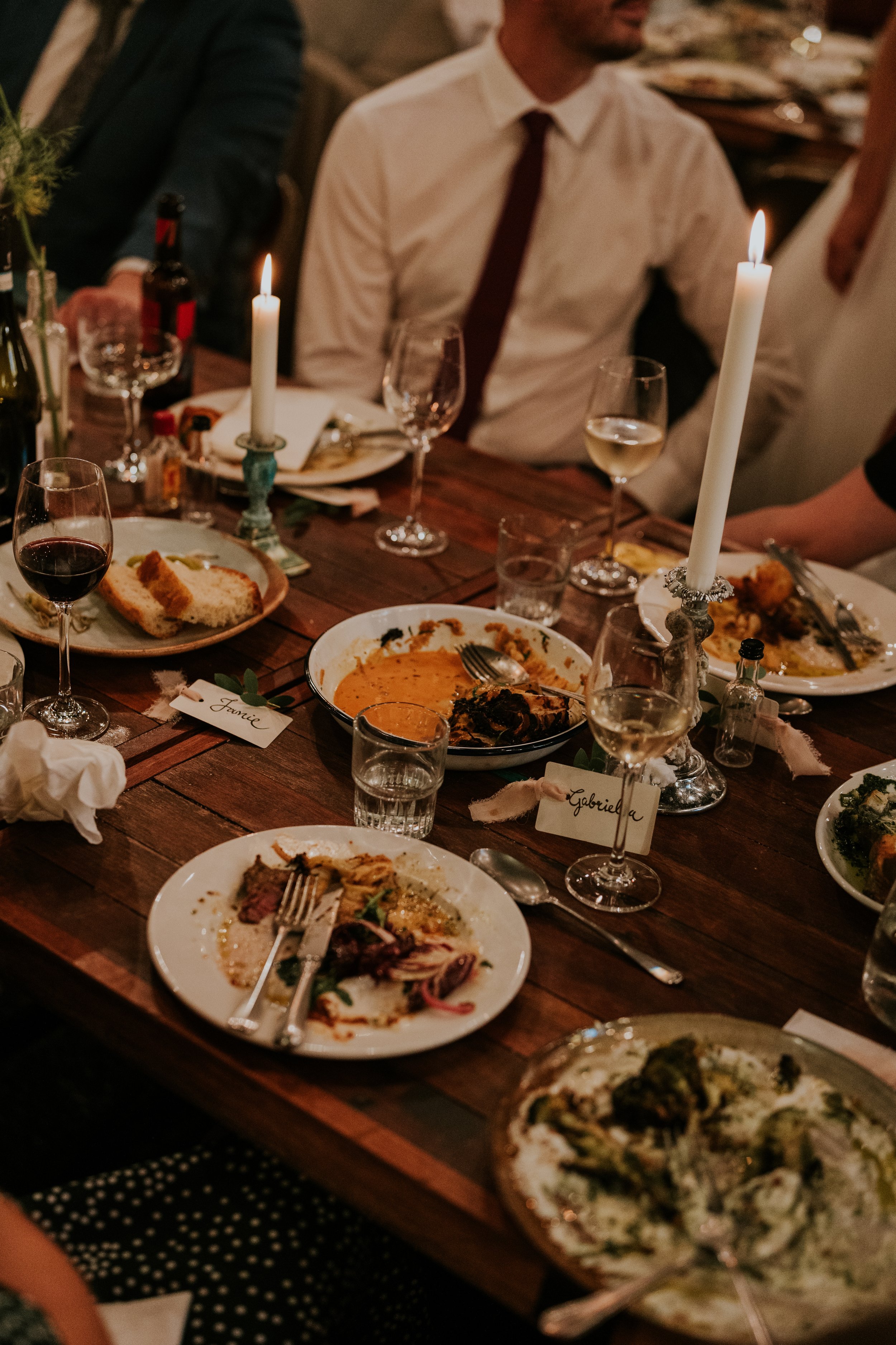 Dinner table set with plates of food, glasses of wine, bread, candles, and name cards at an event.