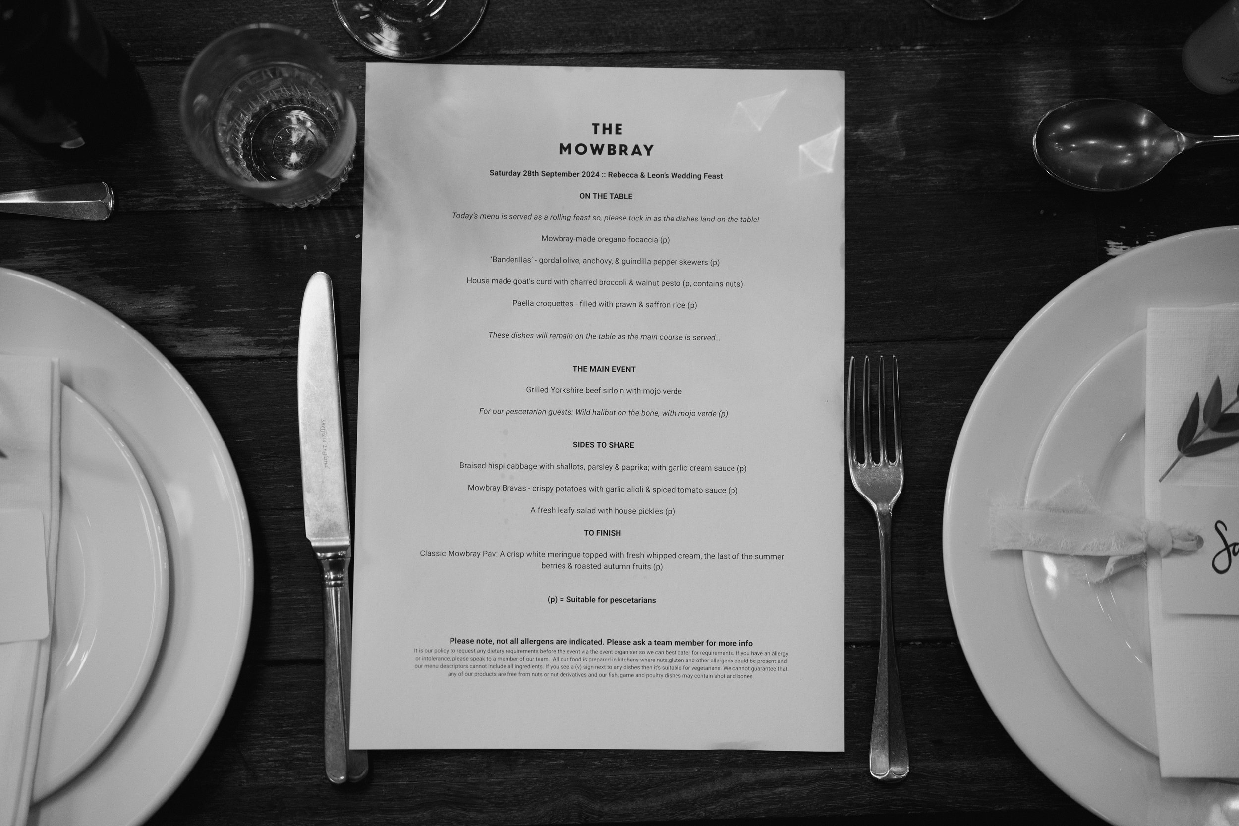 Wedding feast menu on a table with plates, fork, knife, spoon, and glass in black and white.