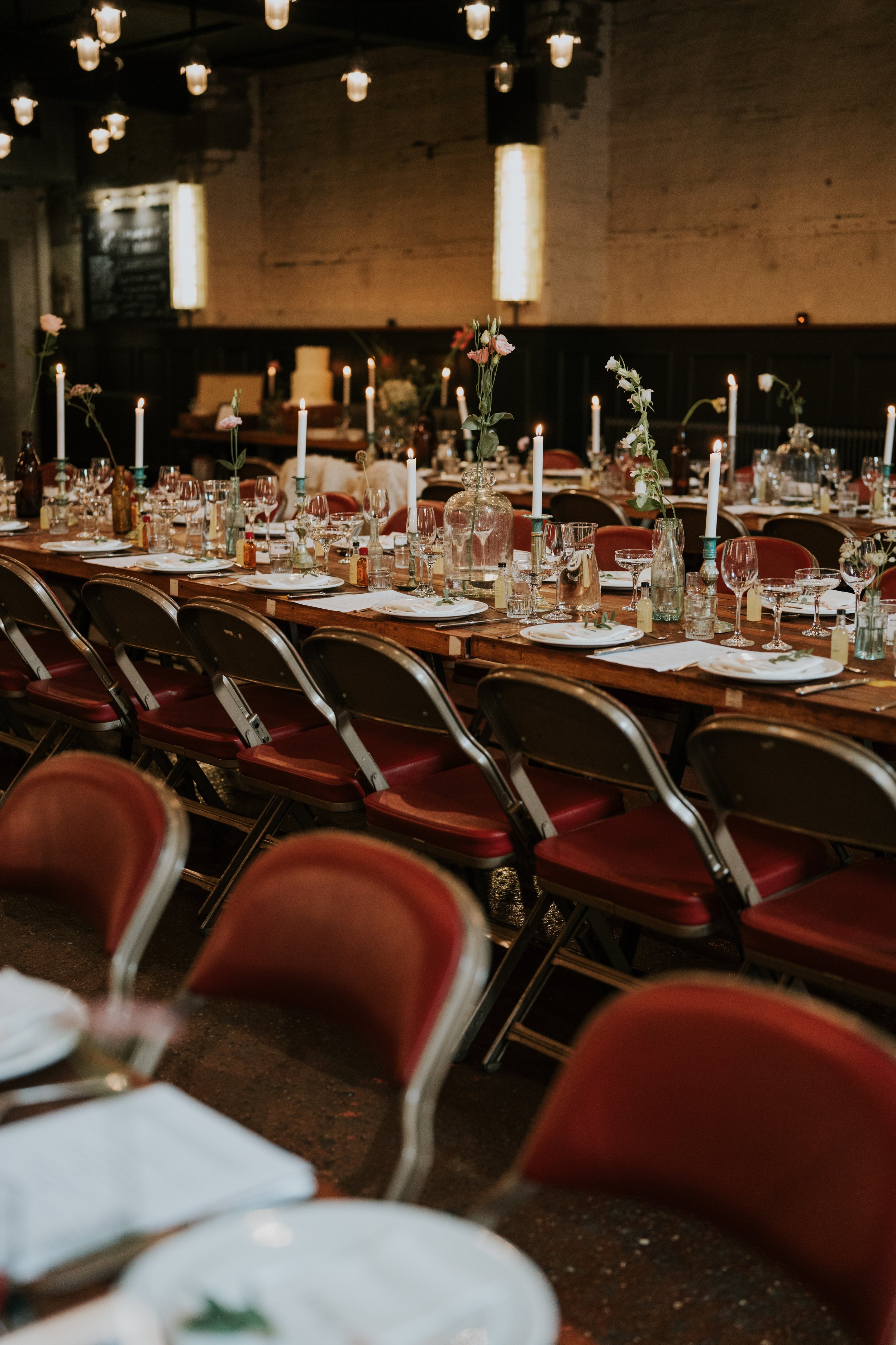 Elegant dining setup with long tables, red chairs, candlesticks, and wine glasses.