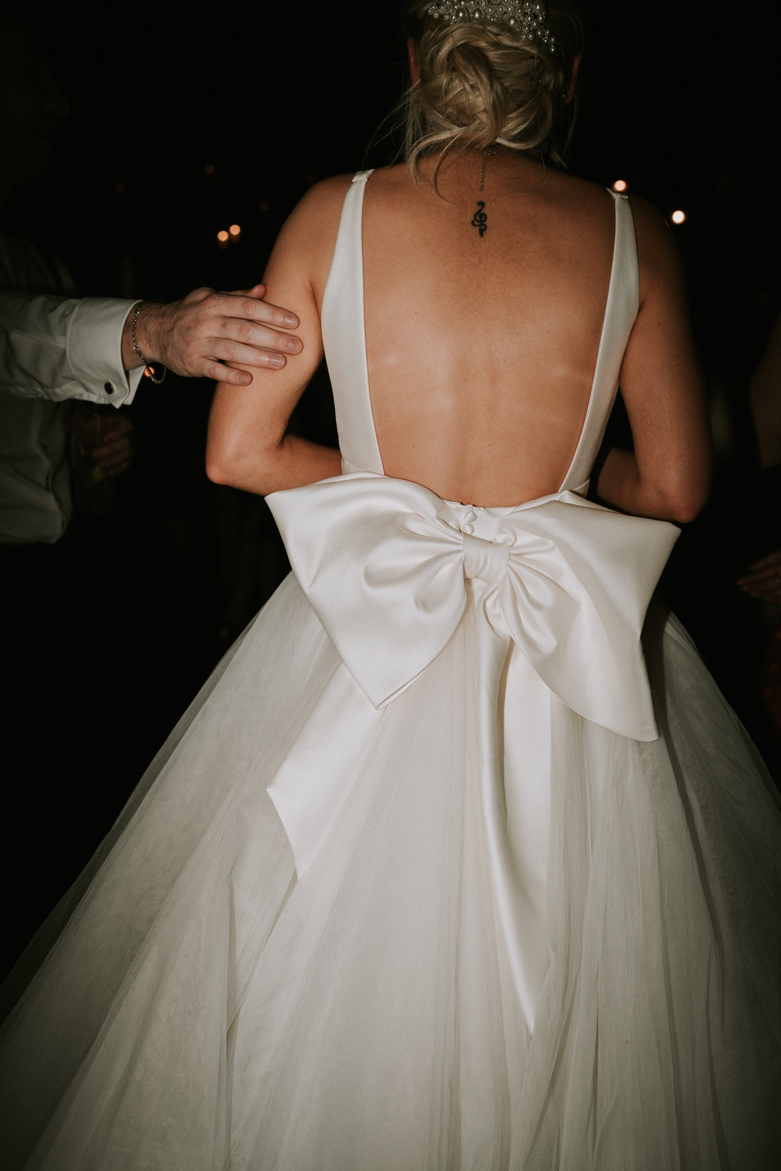Bride in white dress with bow, dark background.