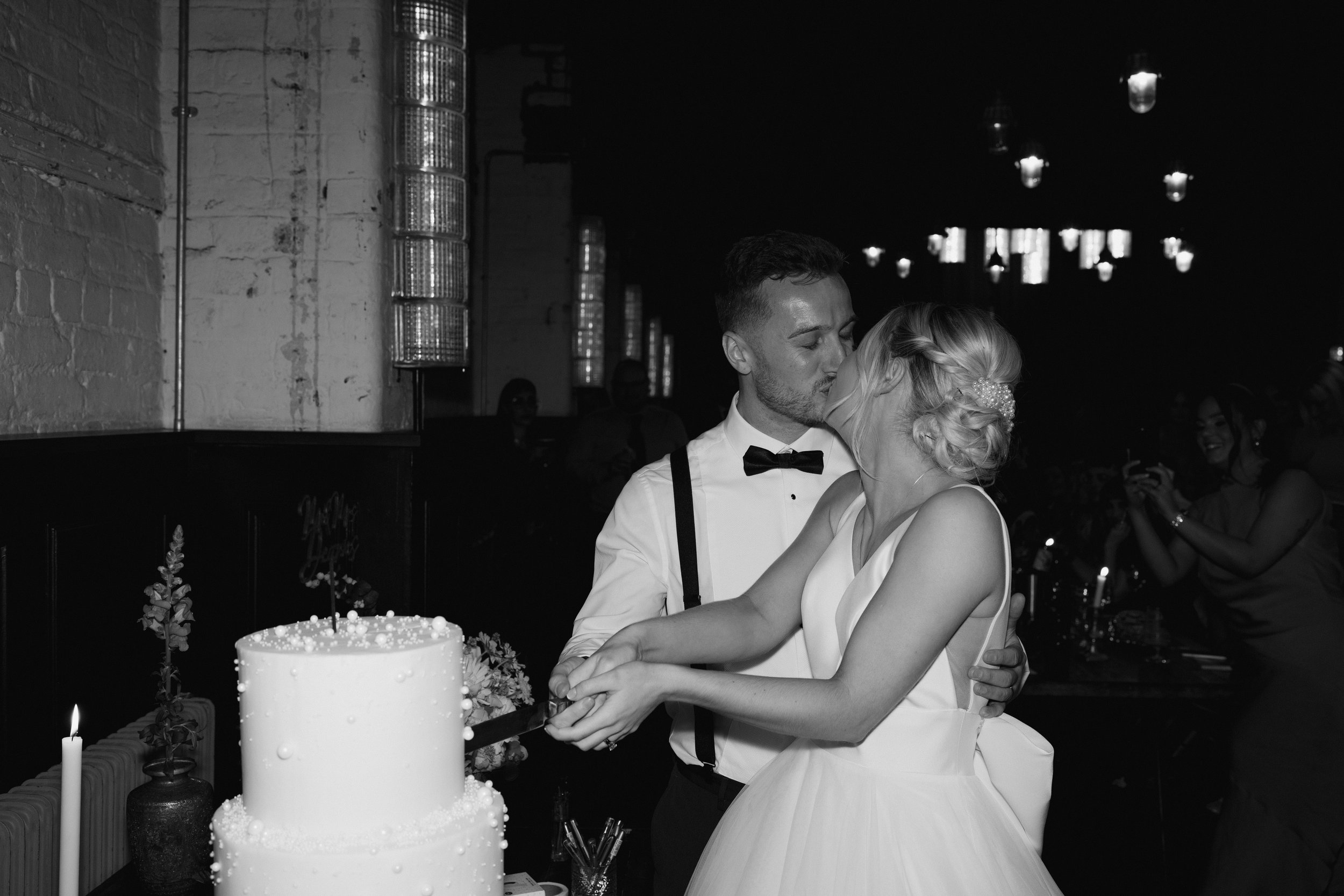 Bride and groom kissing while cutting wedding cake, wedding reception, black and white photo.