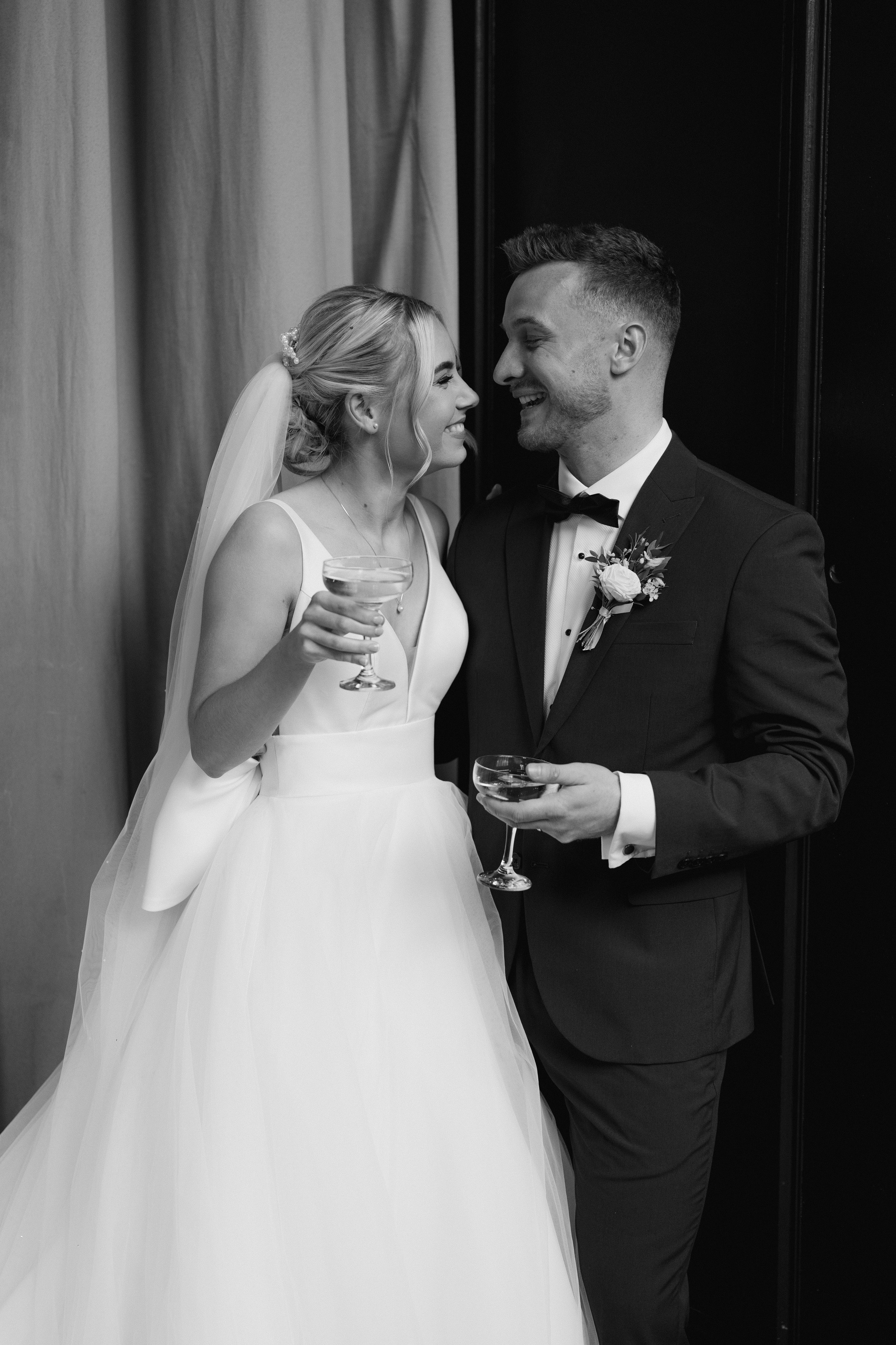 Black and white photo of a bride and groom smiling with glasses in hand.