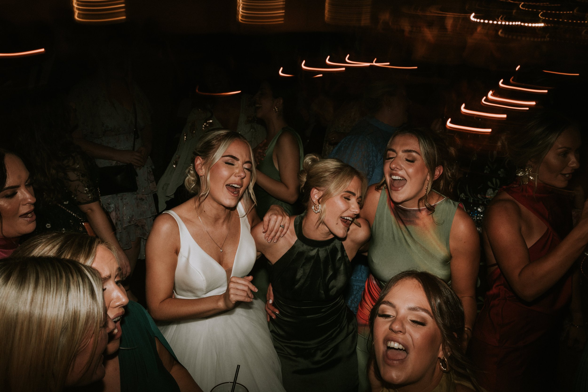 Group of women singing and dancing at a party with a vibrant, lively atmosphere.