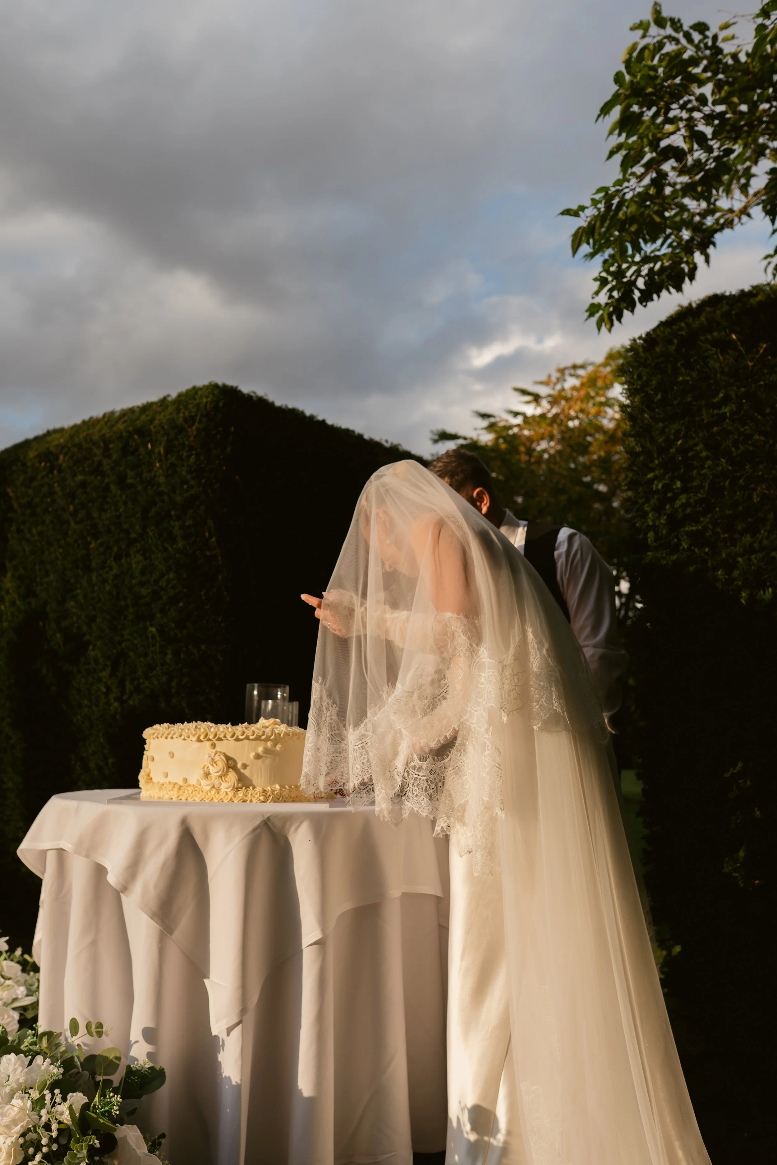 Bride and groom cutting wedding cake outdoors during sunset.