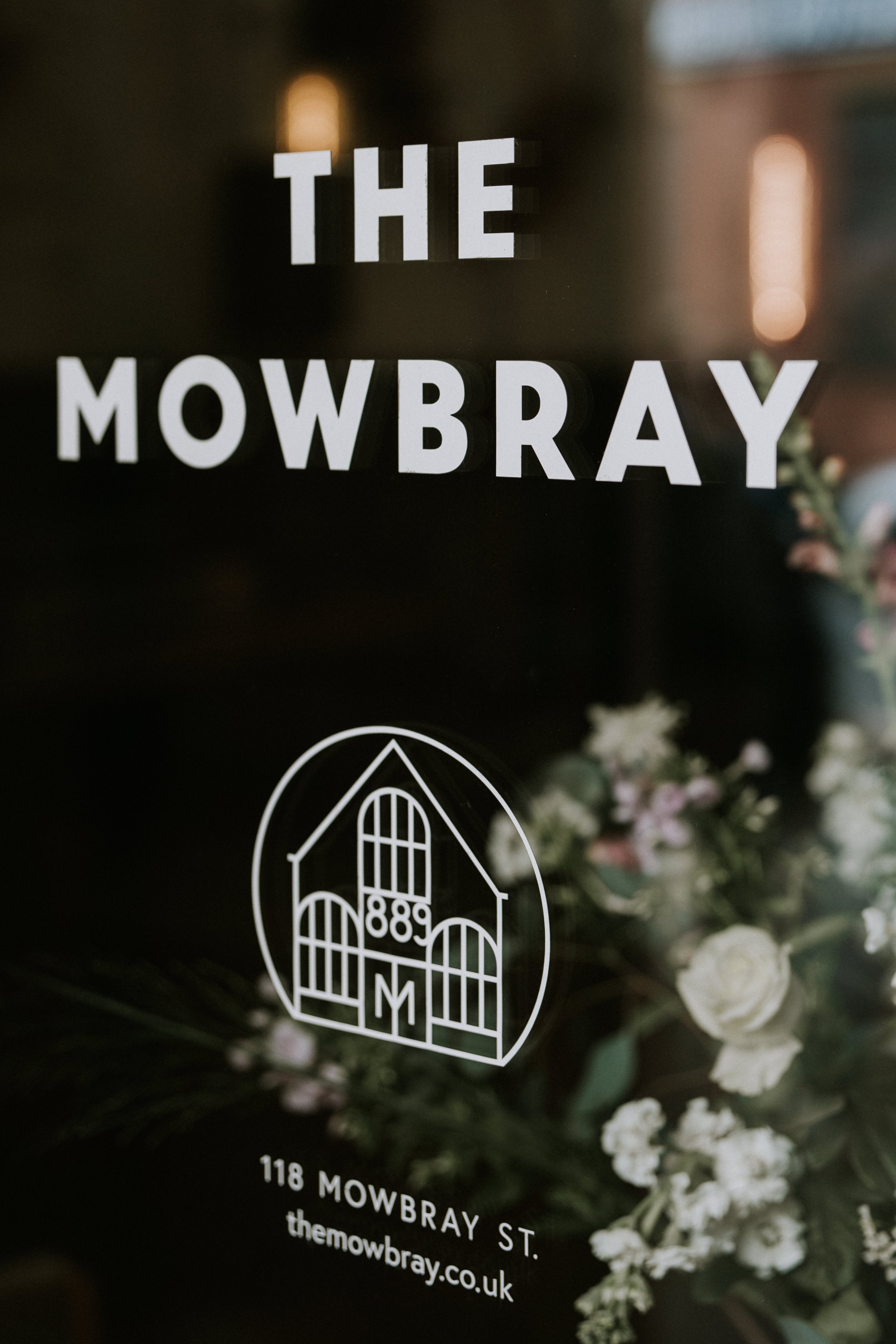 Window sign for The Mowbray with floral background; includes address and website.