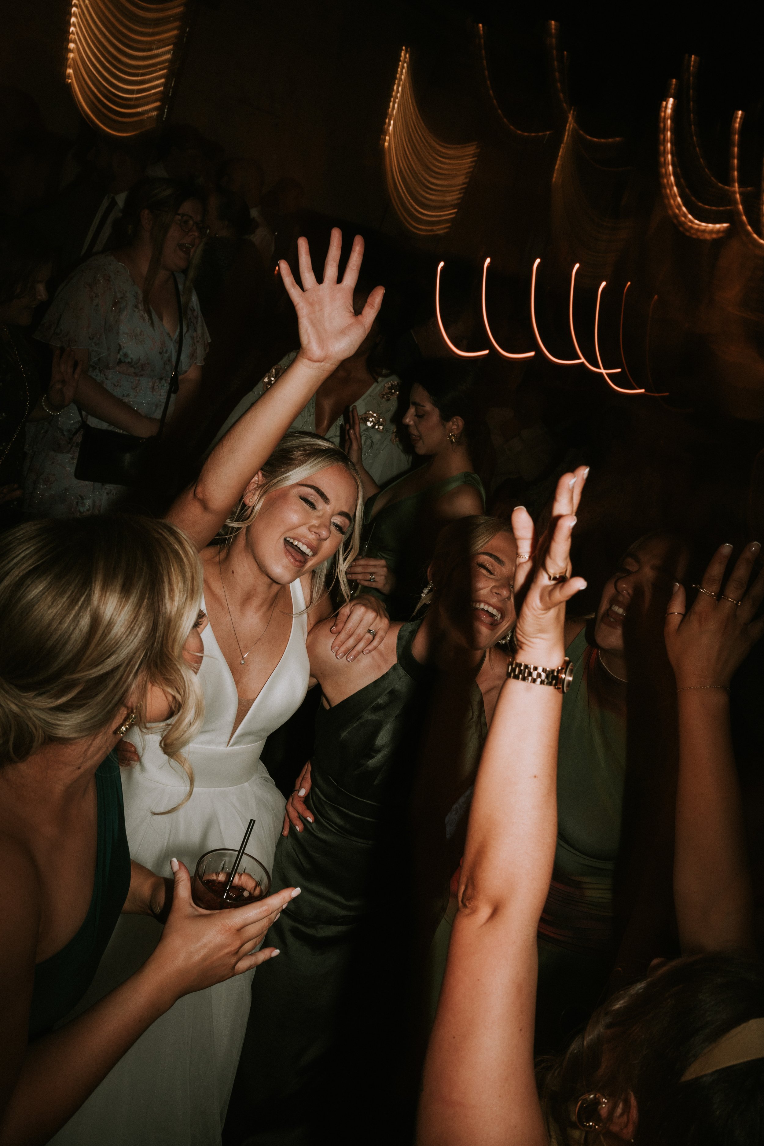 Group of people dancing at a celebration, with a woman in a white dress raising her arms and smiling.