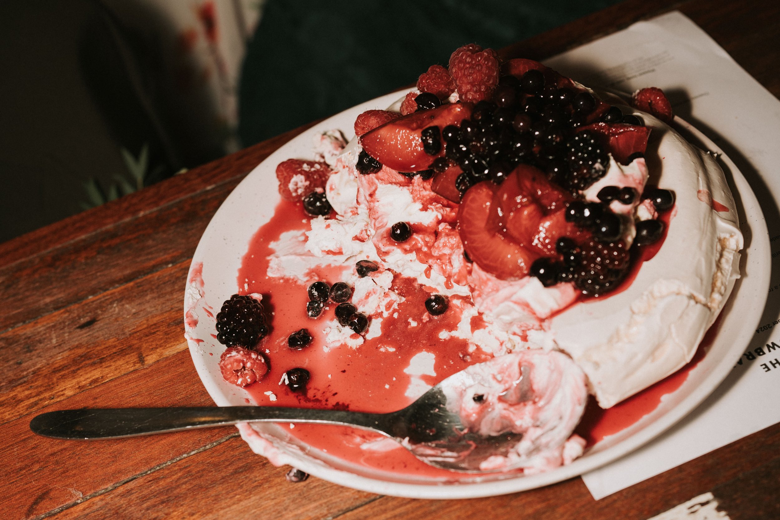 Pavlova dessert topped with mixed berries and fruit sauce on a white plate