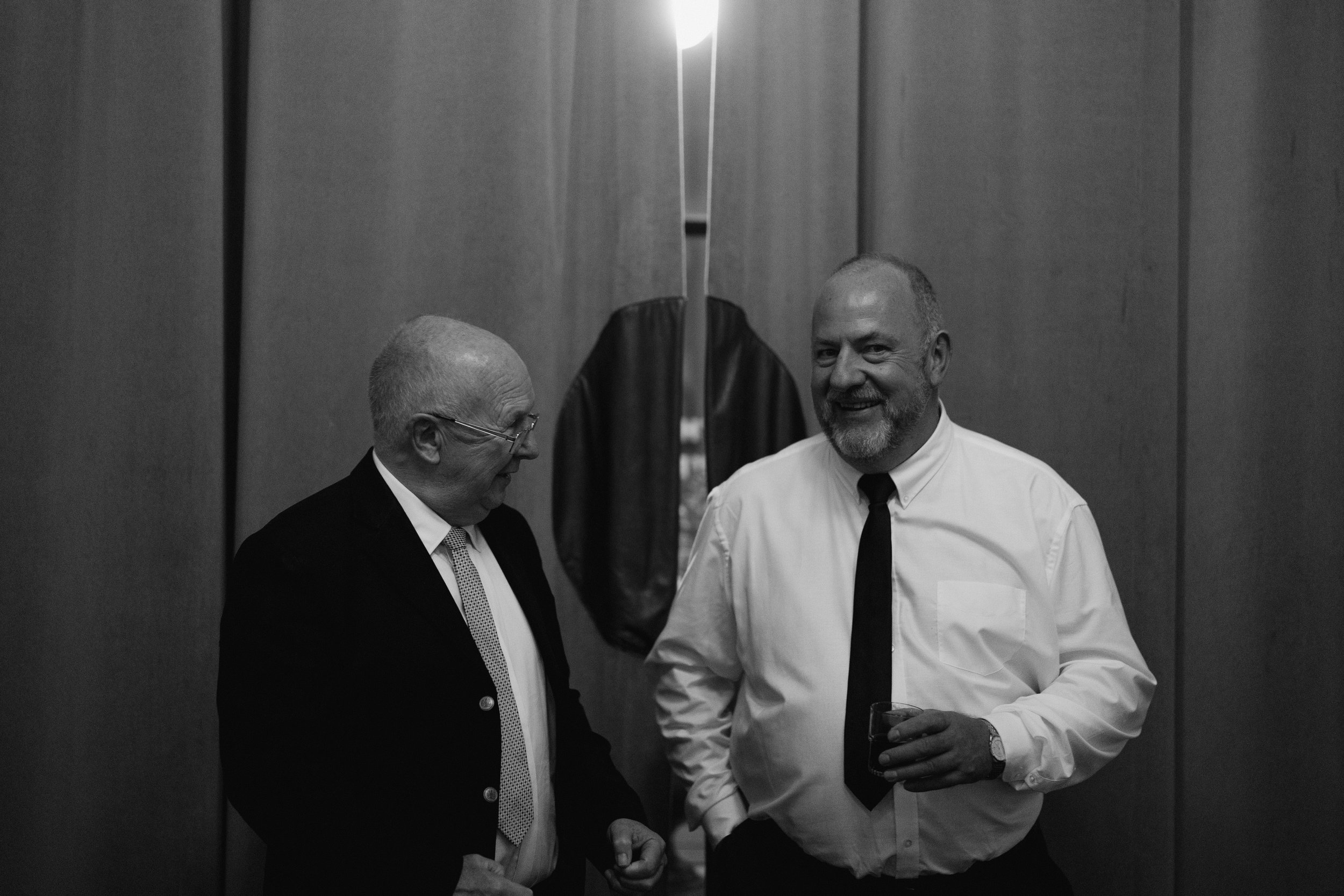 Two men in formal attire talking and smiling in a black and white photograph.