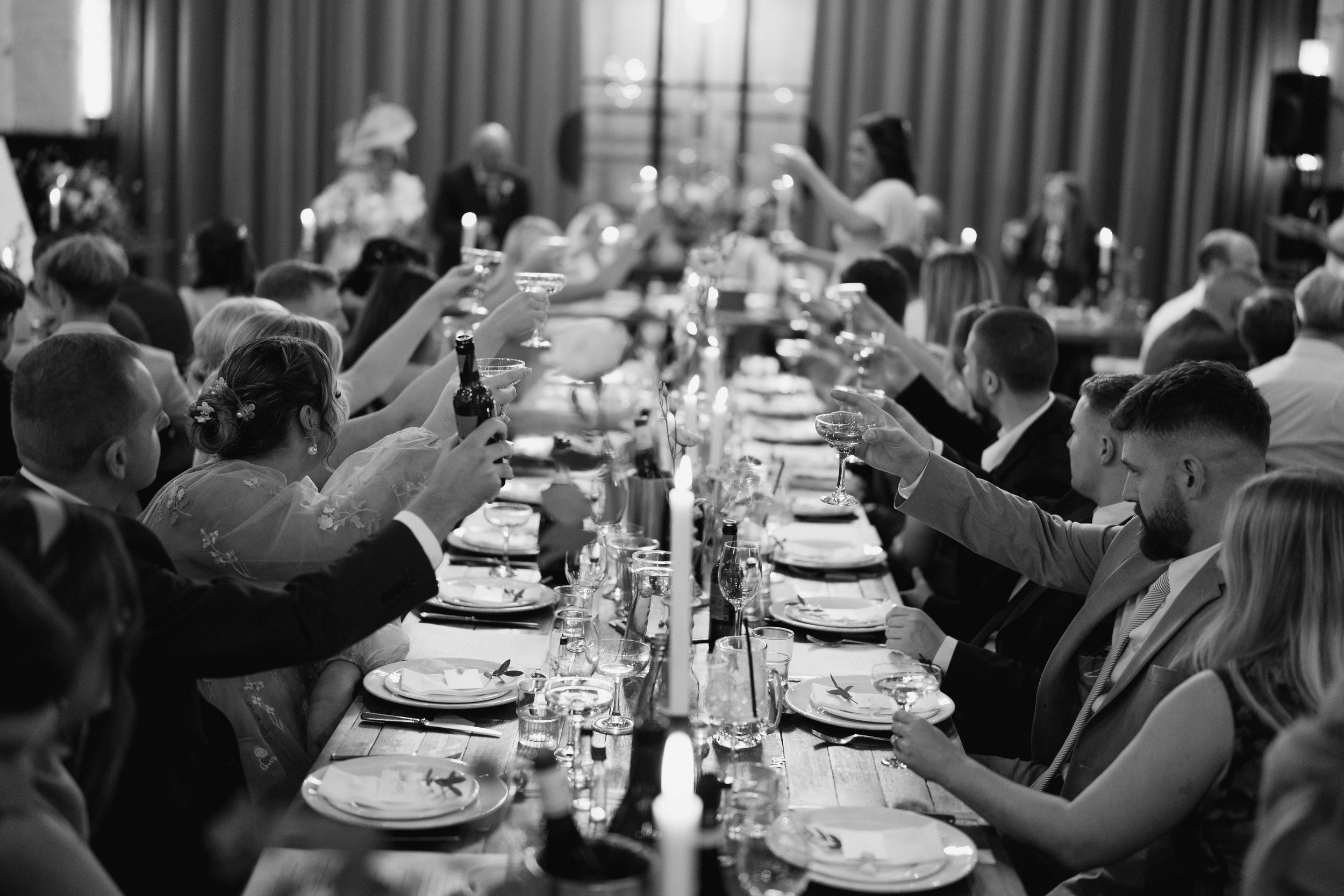 Black and white photo of a formal dinner party, guests raising glasses in a toast around a long table.