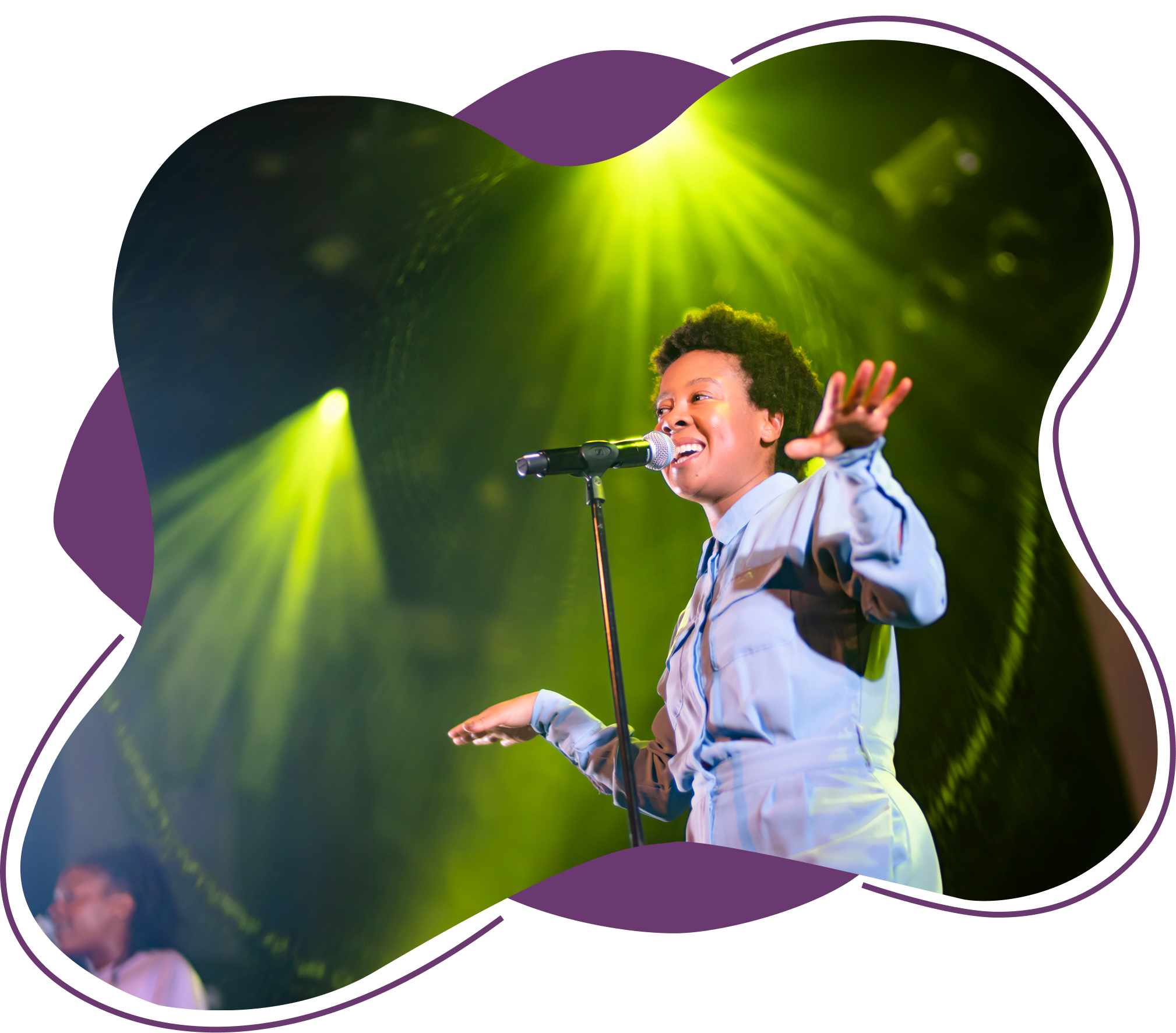 En kvinne synger eller snakker foran mikrofon på scenen med grønne og gule lys bak henne.