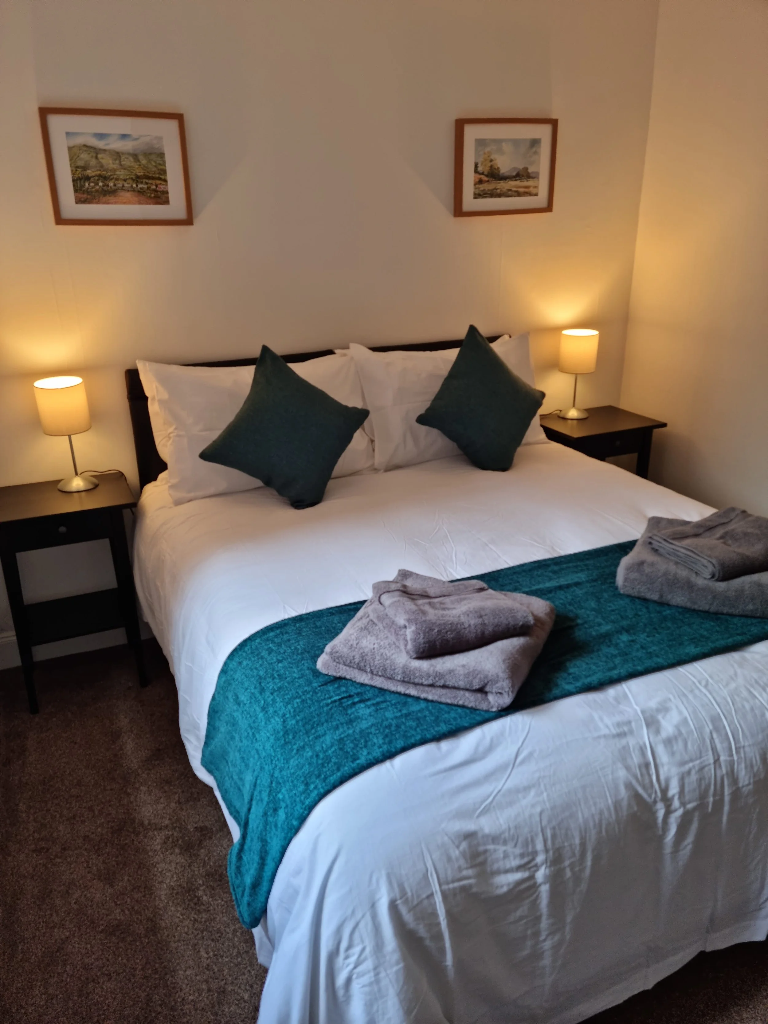 King sized bed with white bedding, green square cushions, green throw and bedside lamps on black tables