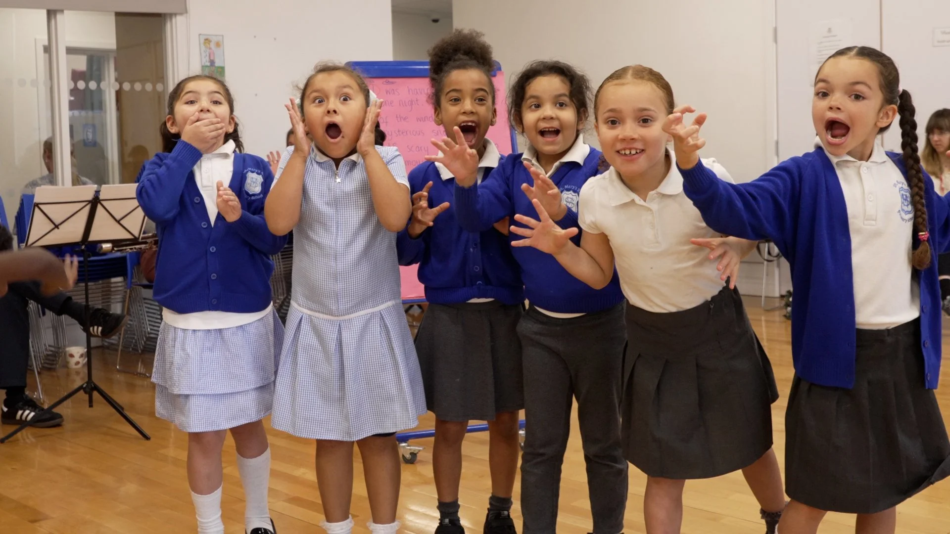 A group of six young girls wearing school uniforms shows surprise and excitement at a school event.
