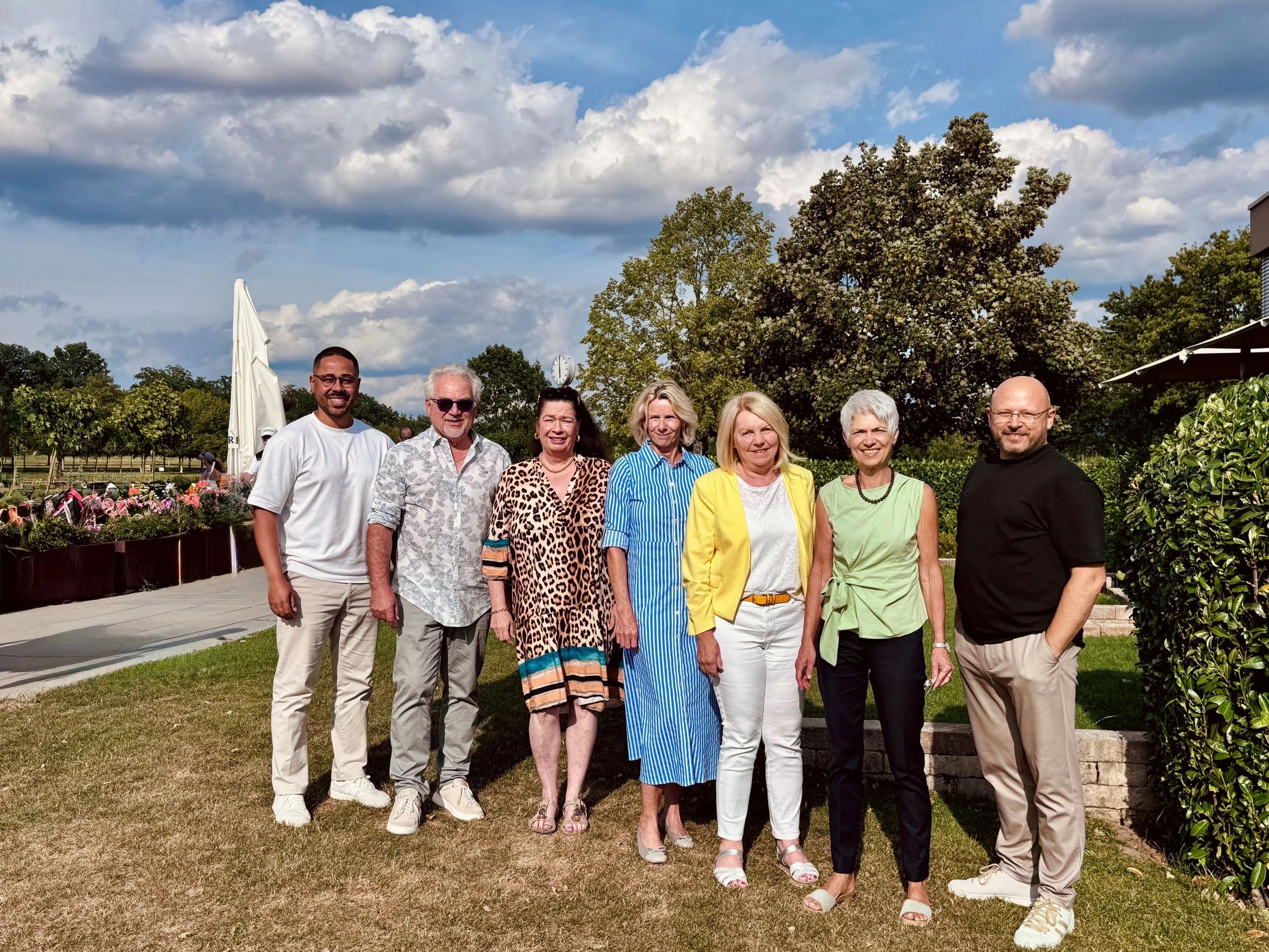 Ein Gruppenbild des gesamten Teams auf einer grünen Wies vor Bäumen und einem blauen Himmel. Es sind 4 Frauen und 3 Männer.