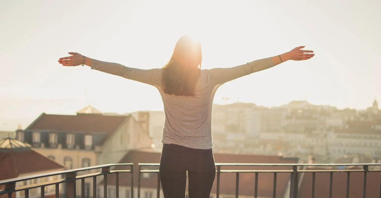 a woman standing on a sunlit terrace with arms outstretched