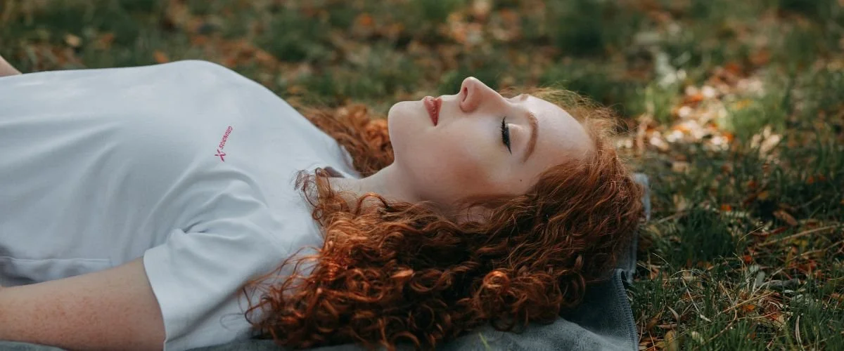 woman with eyes closed laying on blanket on top of grassy field