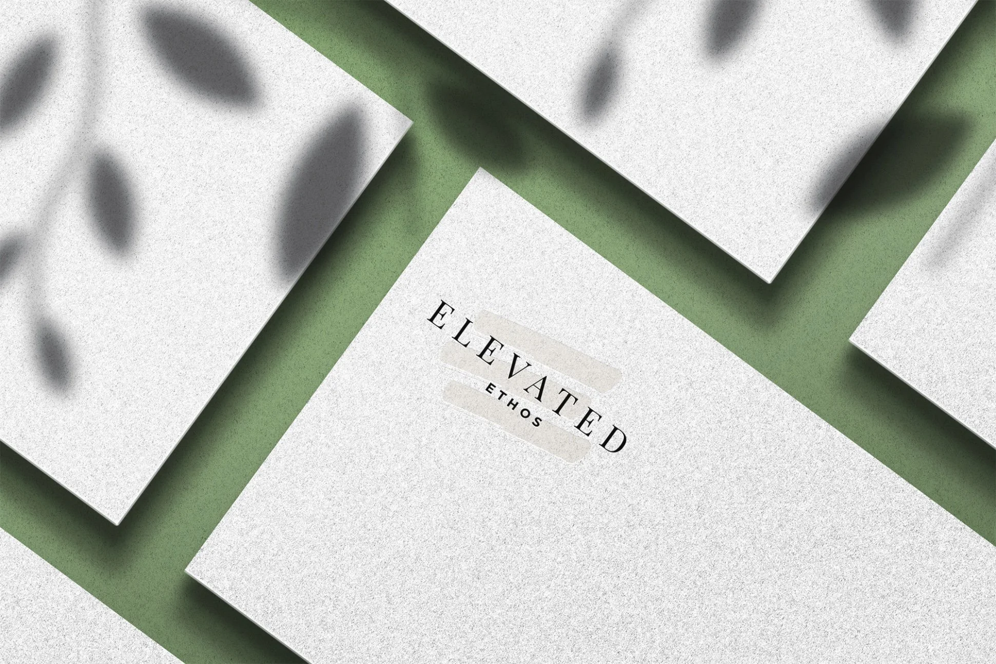 Close-up of layered papers with bold black text that reads "ELEVATE D ETHOS" on a white sheet, with shadowed pieces on a green background.