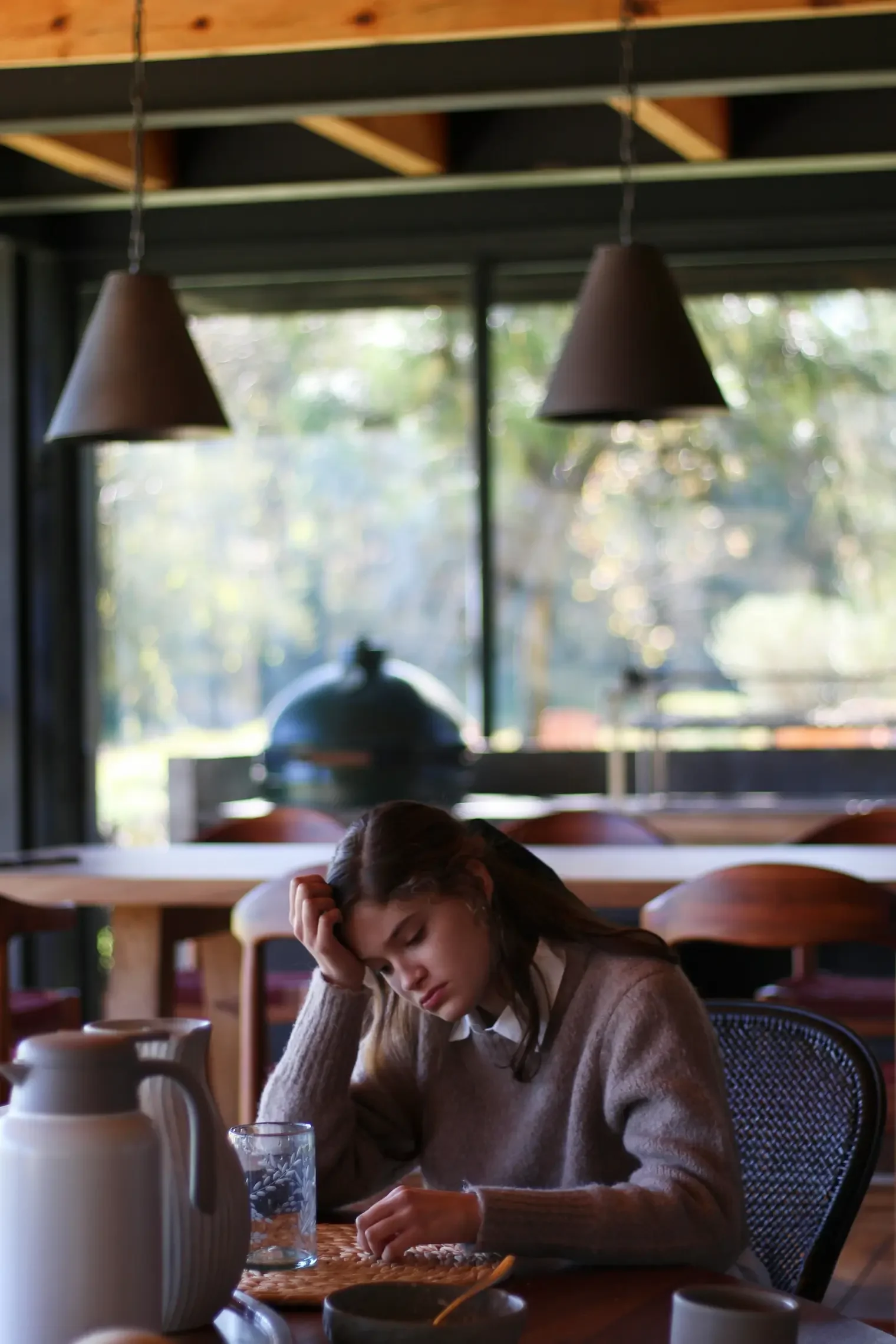 Teen girl sitting at a table with her head resting in her hand, appearing worried and emotionally overwhelmed.