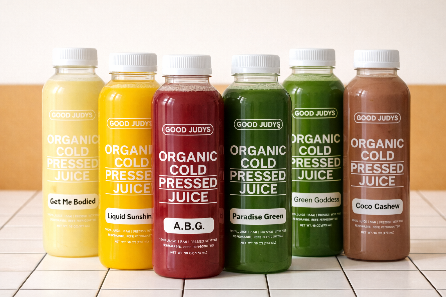 Five bottles of organic cold-pressed juice in yellow, red, green, and brown colors, each labeled with different flavors.
