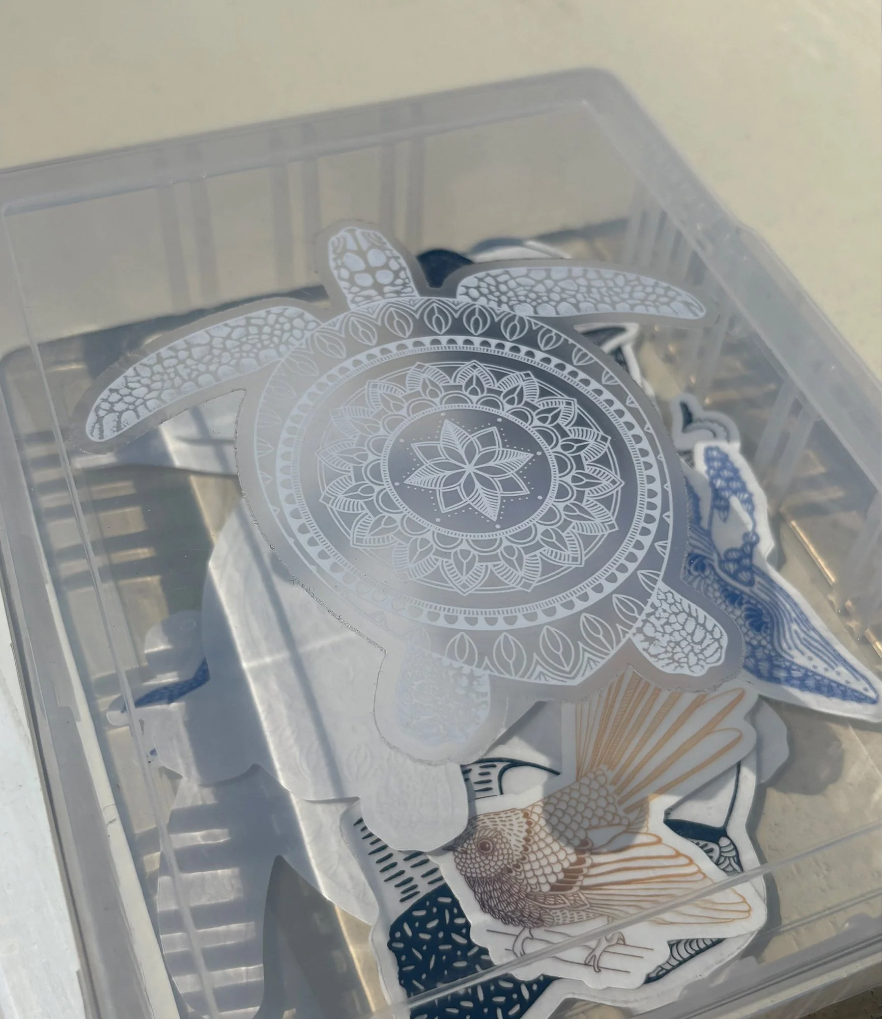 Vinyl sticker with a clear background featuring a drawing of a turtle with a mandala pattern on its shell. Unique ocean art encapsulated into a durable, waterproof sticker.