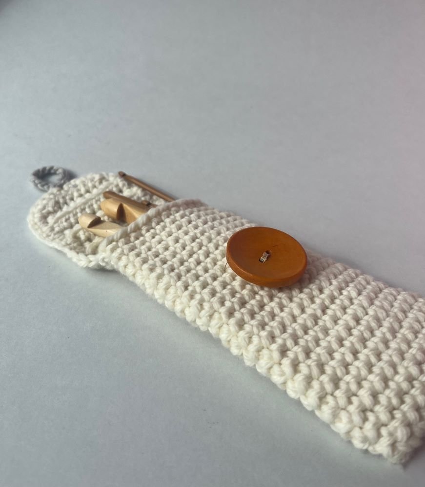 Handmade wool crochet case with wooden button, neatly folded to show compact design for crafting tools.
