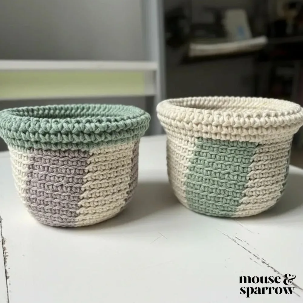 Modern crochet basket with folded edge detail sitting on a white table filled with pens and craft supplies.