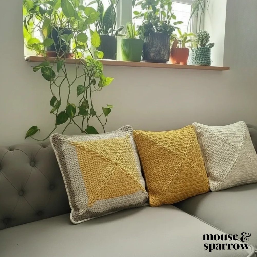 Three crochet pillows on a grey sofa by a window