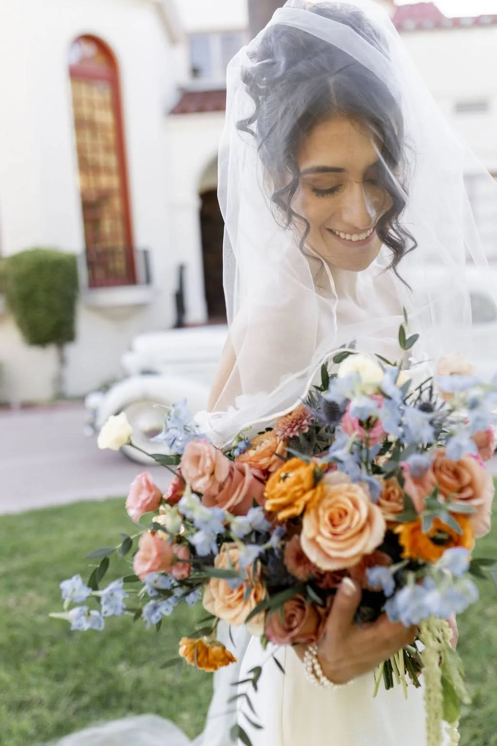 Bride holding a large bouquet of orange, blue, pink, white, and blush-colored flowers.