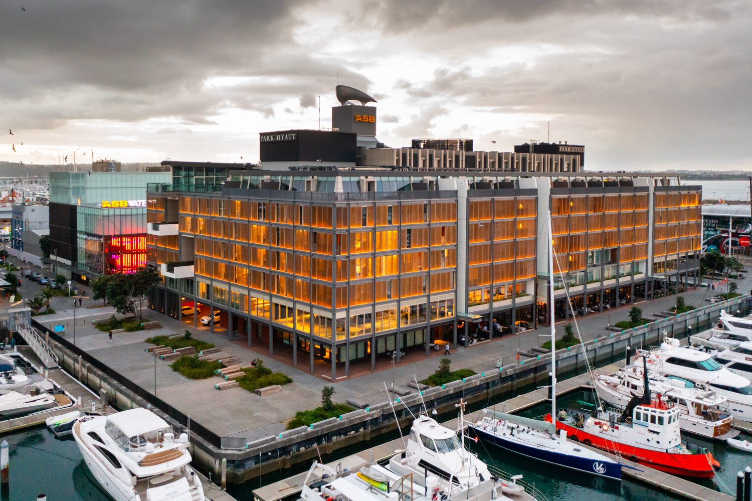 Marina with yachts docked in front of a modern hotel building on a cloudy day.
