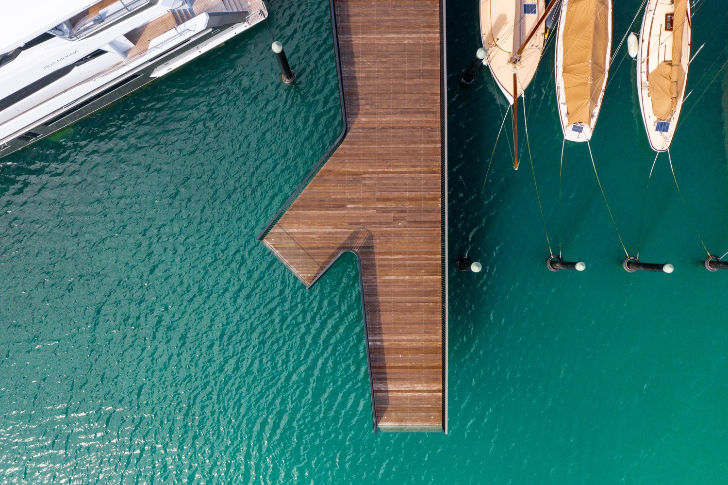 Aerial view of a wooden pier extending over turquoise water, with boats docked alongside.