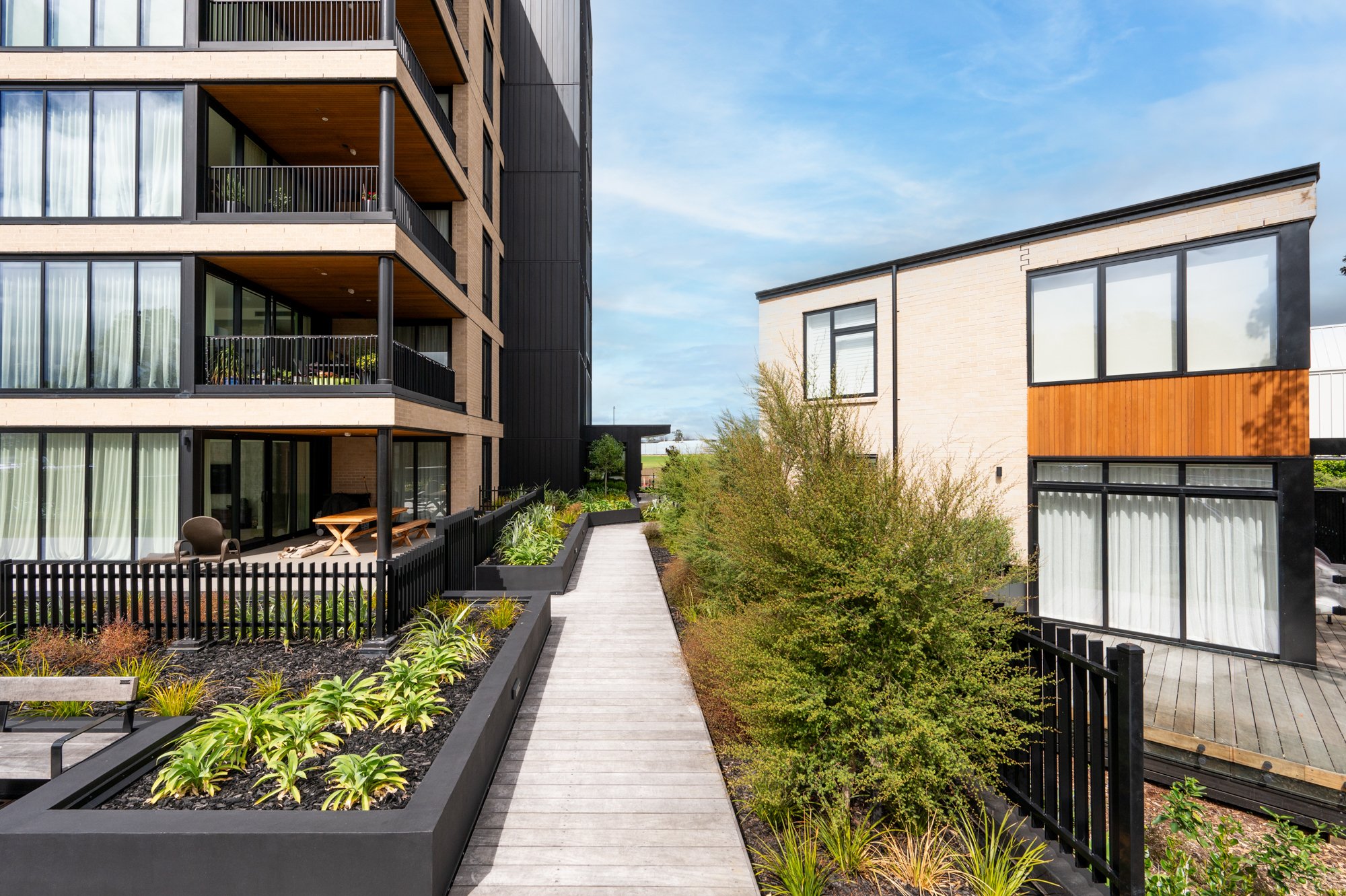 Modern apartment buildings with balconies, a walkway in between, and landscaped planters.