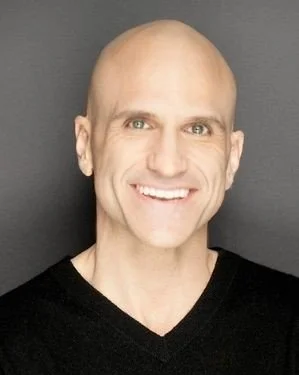 Smiling bald man wearing a black shirt against a gray background