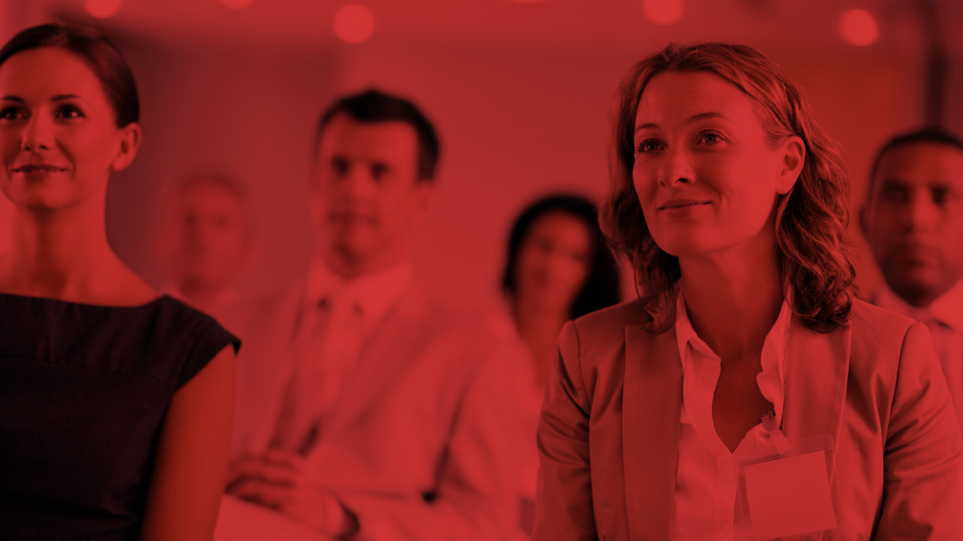 Audience at a conference with a red filter effect, focusing on a woman smiling in the foreground.