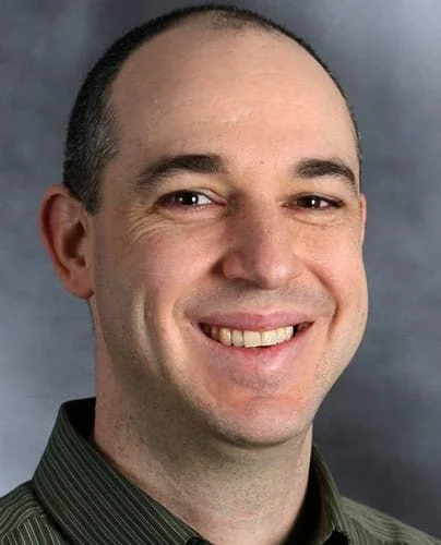 Smiling man wearing a dark green shirt against a gray background.