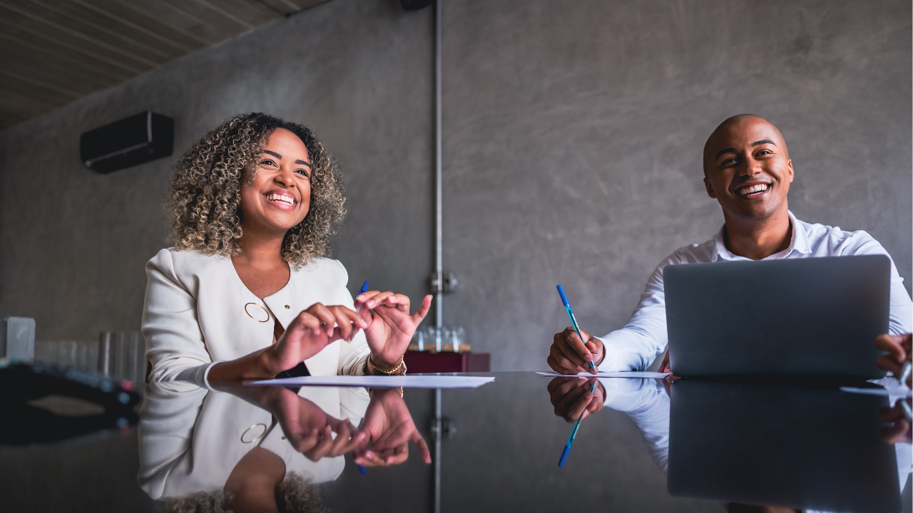 co-worker man and women sitting at a table with laptop and notepad smiling