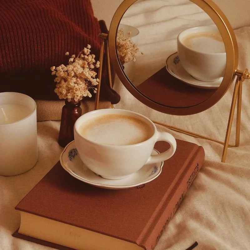 Coffee, book, and candle styled on a bed, representing therapy for perfectionism