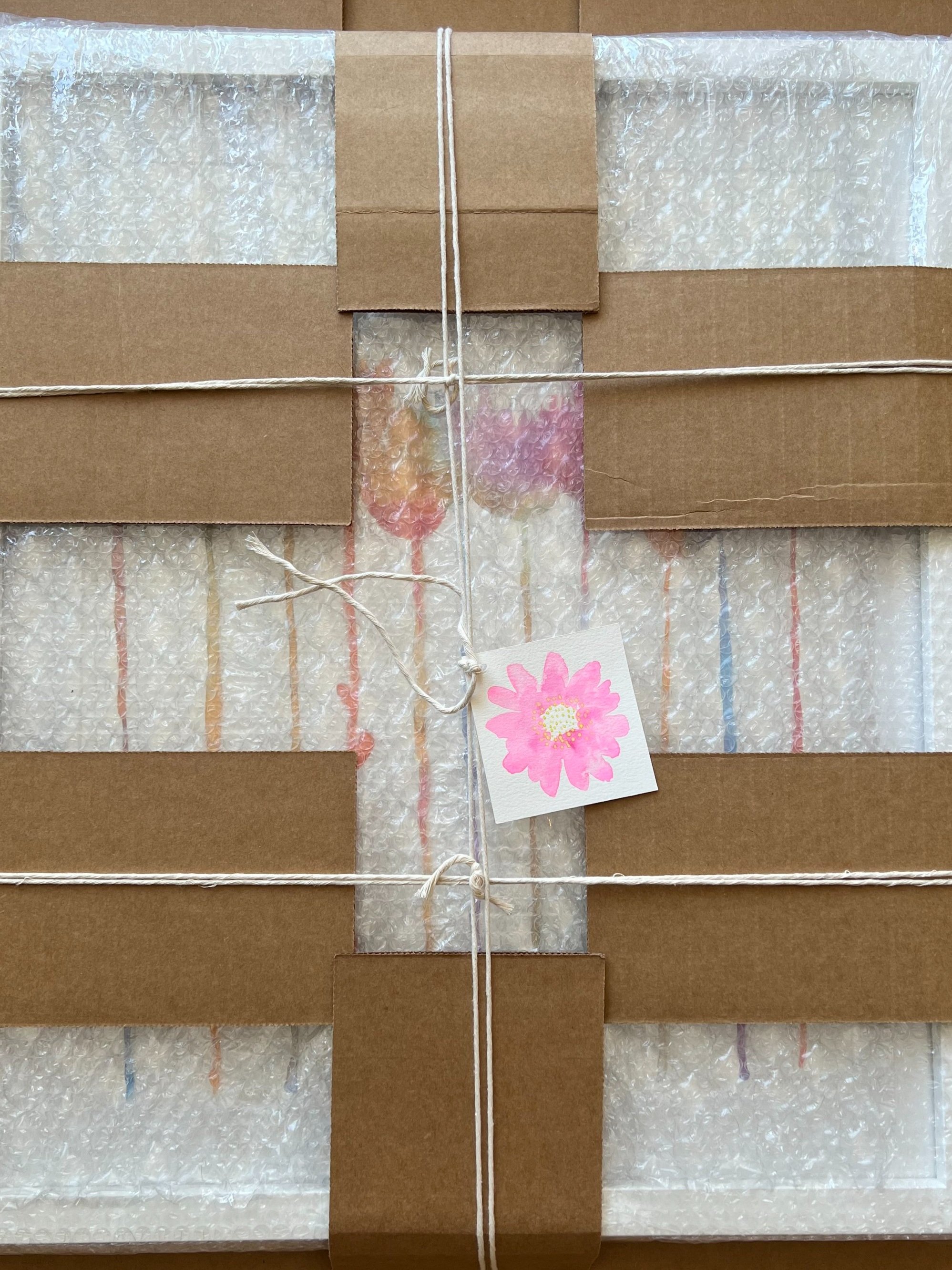 A wrapped package with brown paper, bubble wrap, and white string tied around it, with a pink flower tag attached.