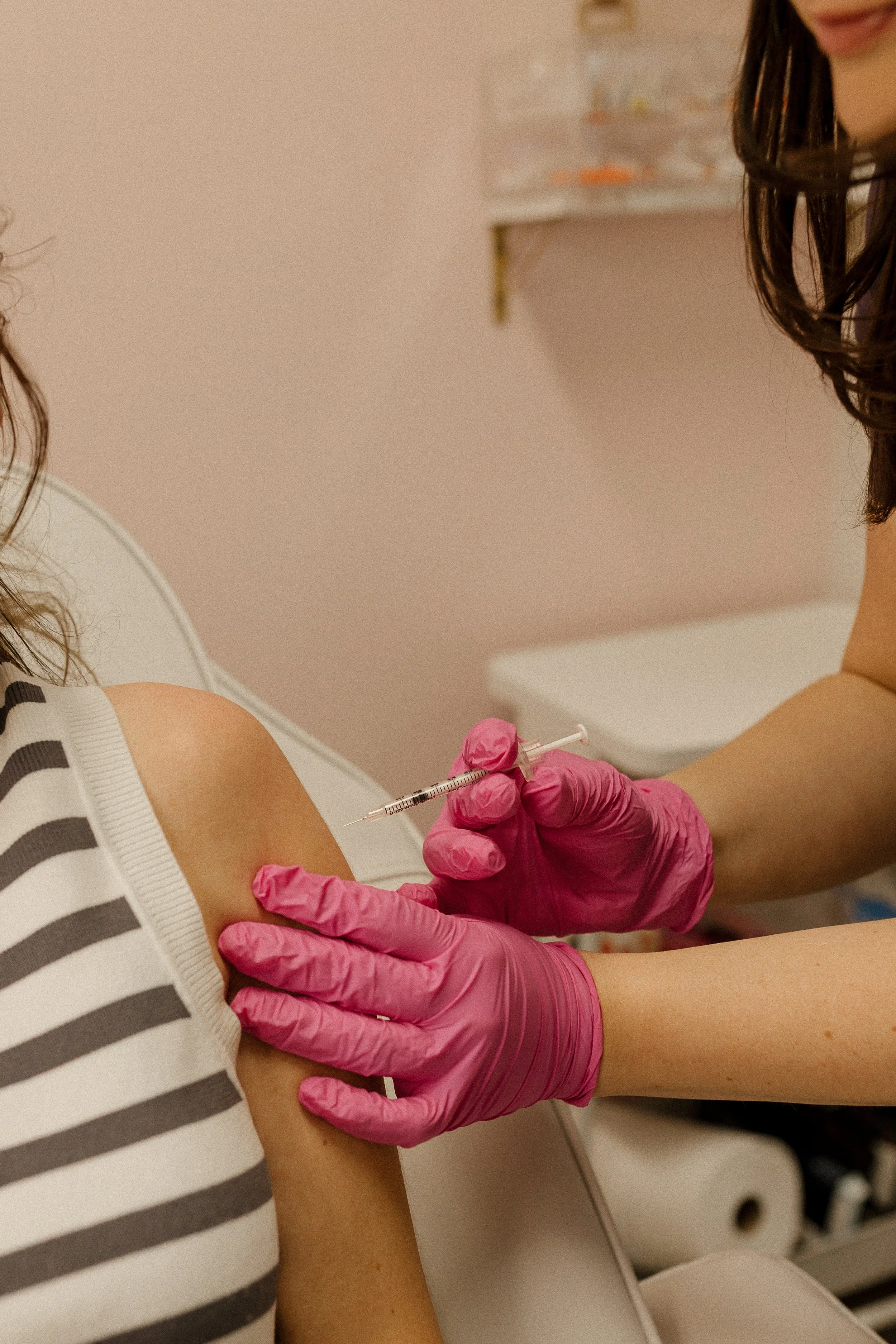 A healthcare professional administering a needle or injection into a patient's arm. The professional is wearing medical scrubs.