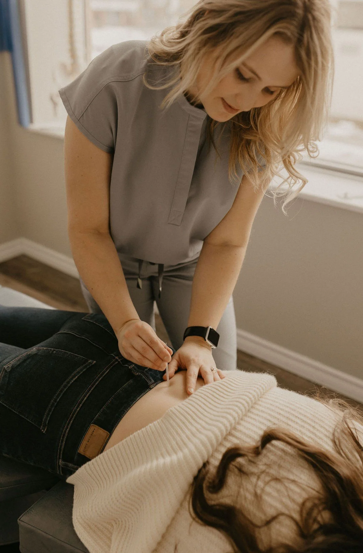 A massage therapist performing a back massage on a client lying face down on a massage table in a therapy room.