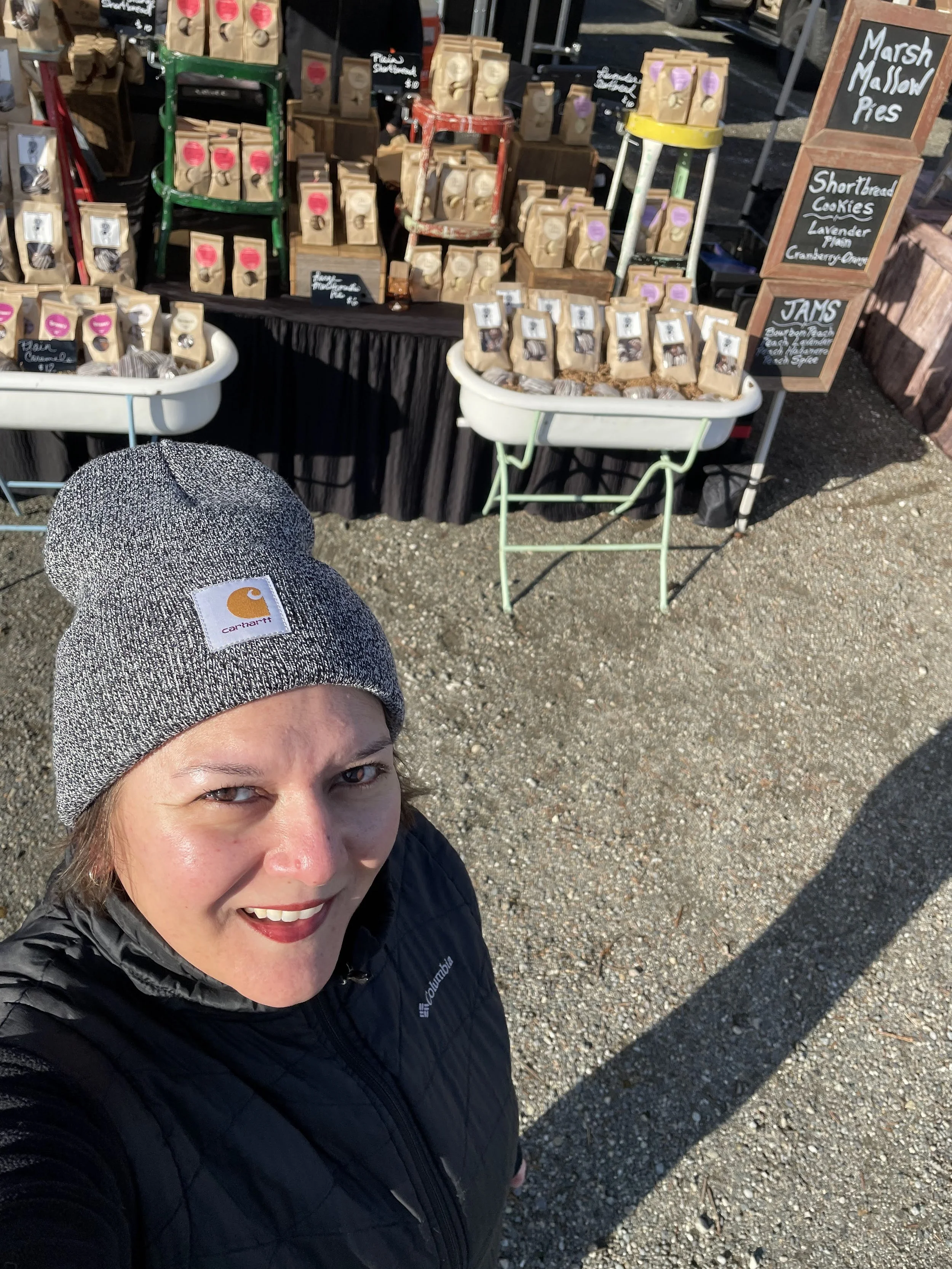 Lorraine taking a selfie at an outdoor market stall selling marshmallow pies and shortbread cookies.