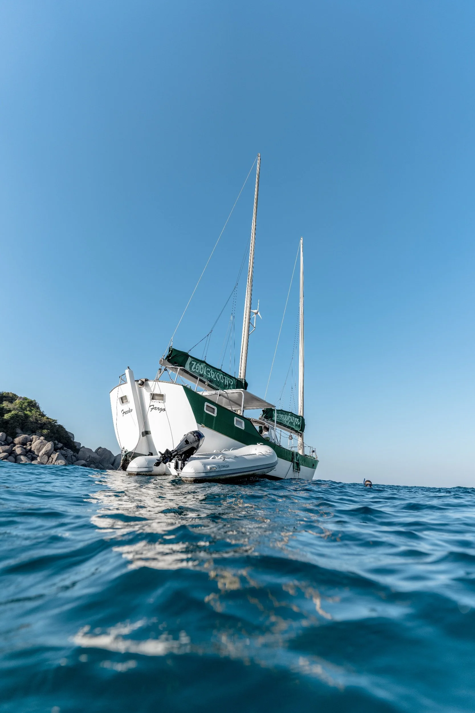 SV Freedom Fargo sailing yacht anchored near rocky coastline of Koh Tao on clear day during Orenda Freediving sailing and ocean training operations