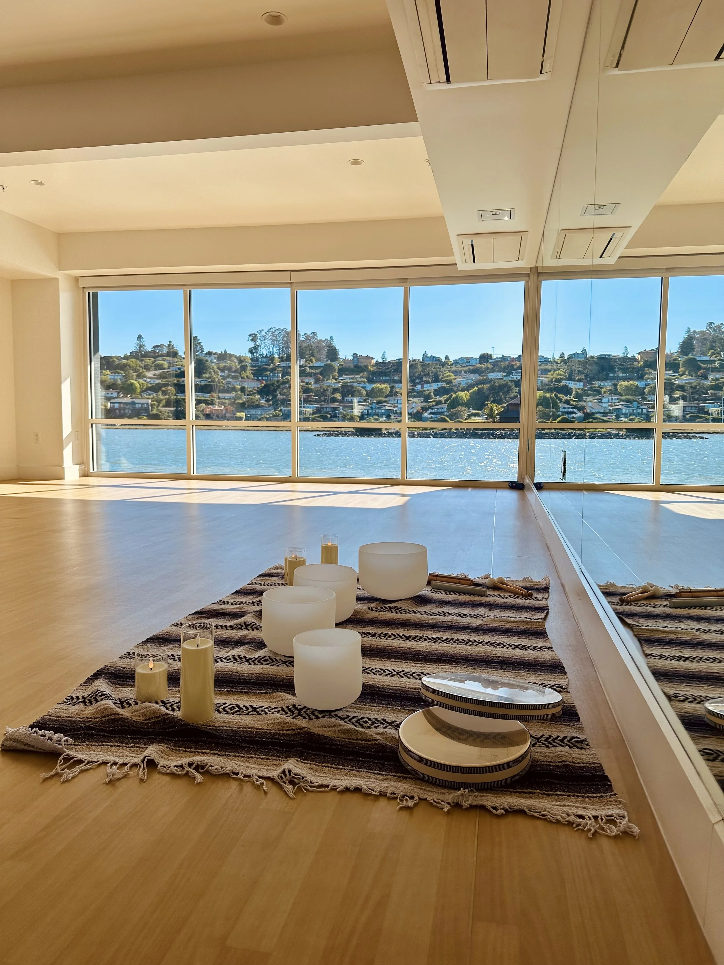 Room with large windows overlooking water, candles on a striped rug, and a mirror wall reflecting the room and view.