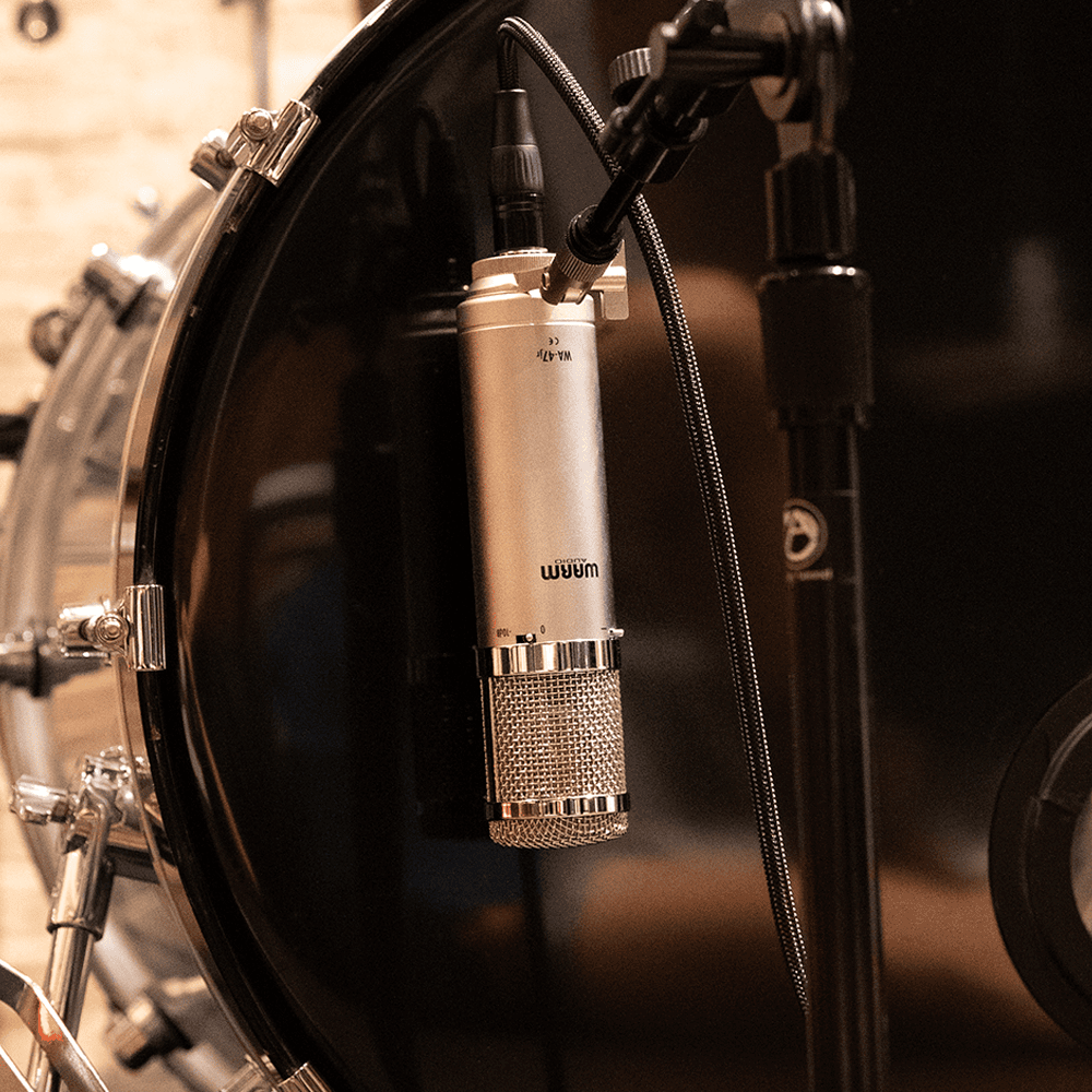Close-up of a condenser microphone mounted inside a drum, with a black drum surface and microphone stand visible.
