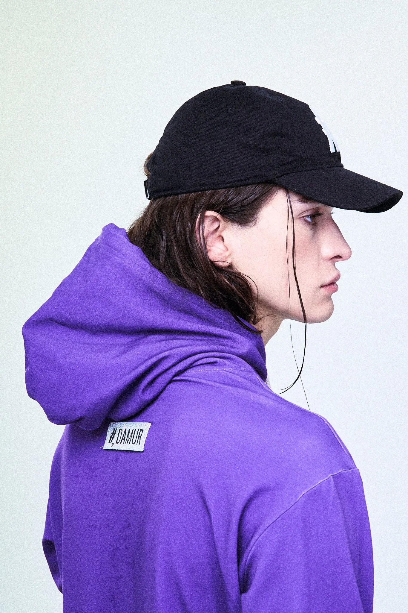 Profile of a person in profile, wearing a black cap and purple hoodie, with a light background.