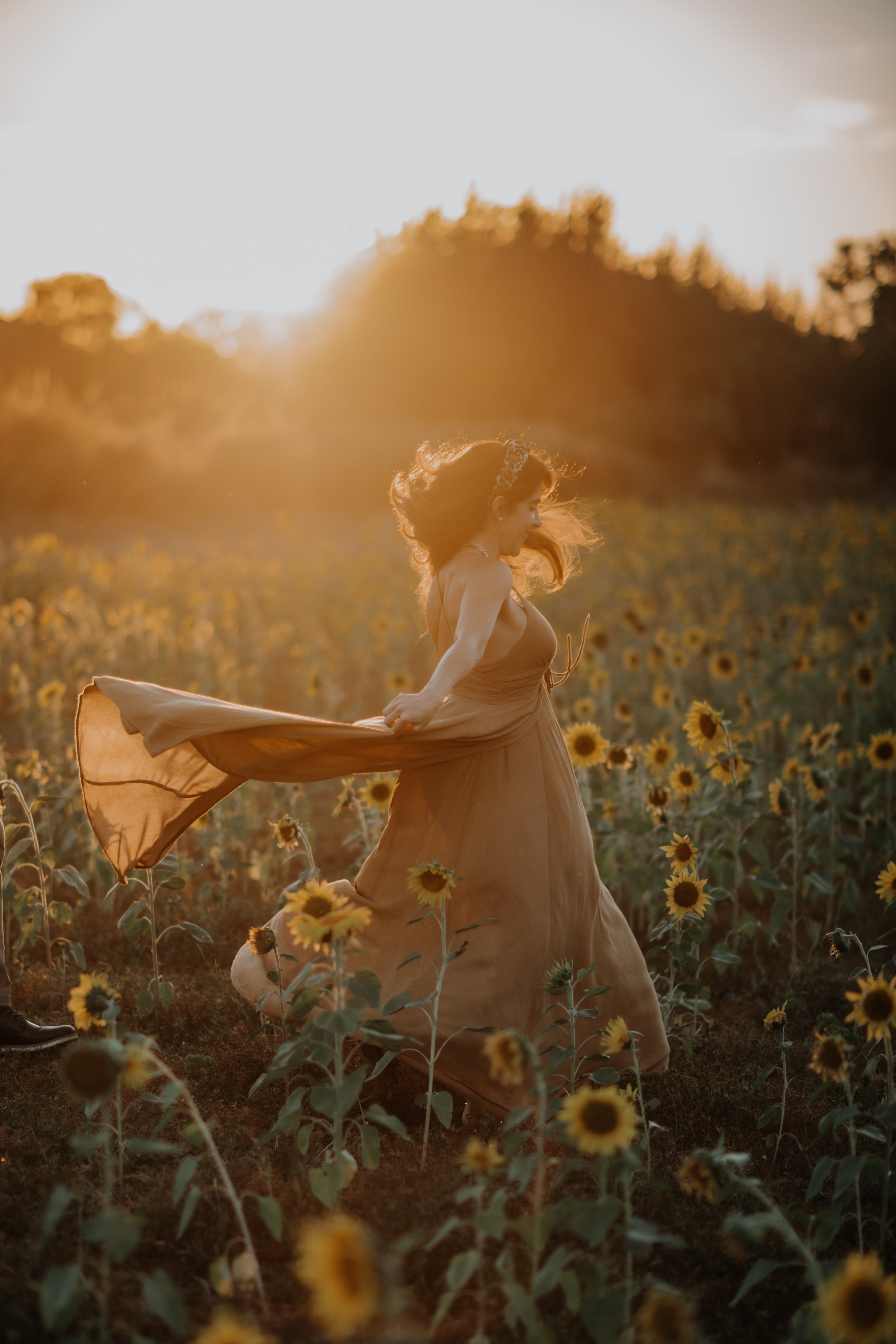 A woman in a flowing dress dancing in a sunflower field at sunset.