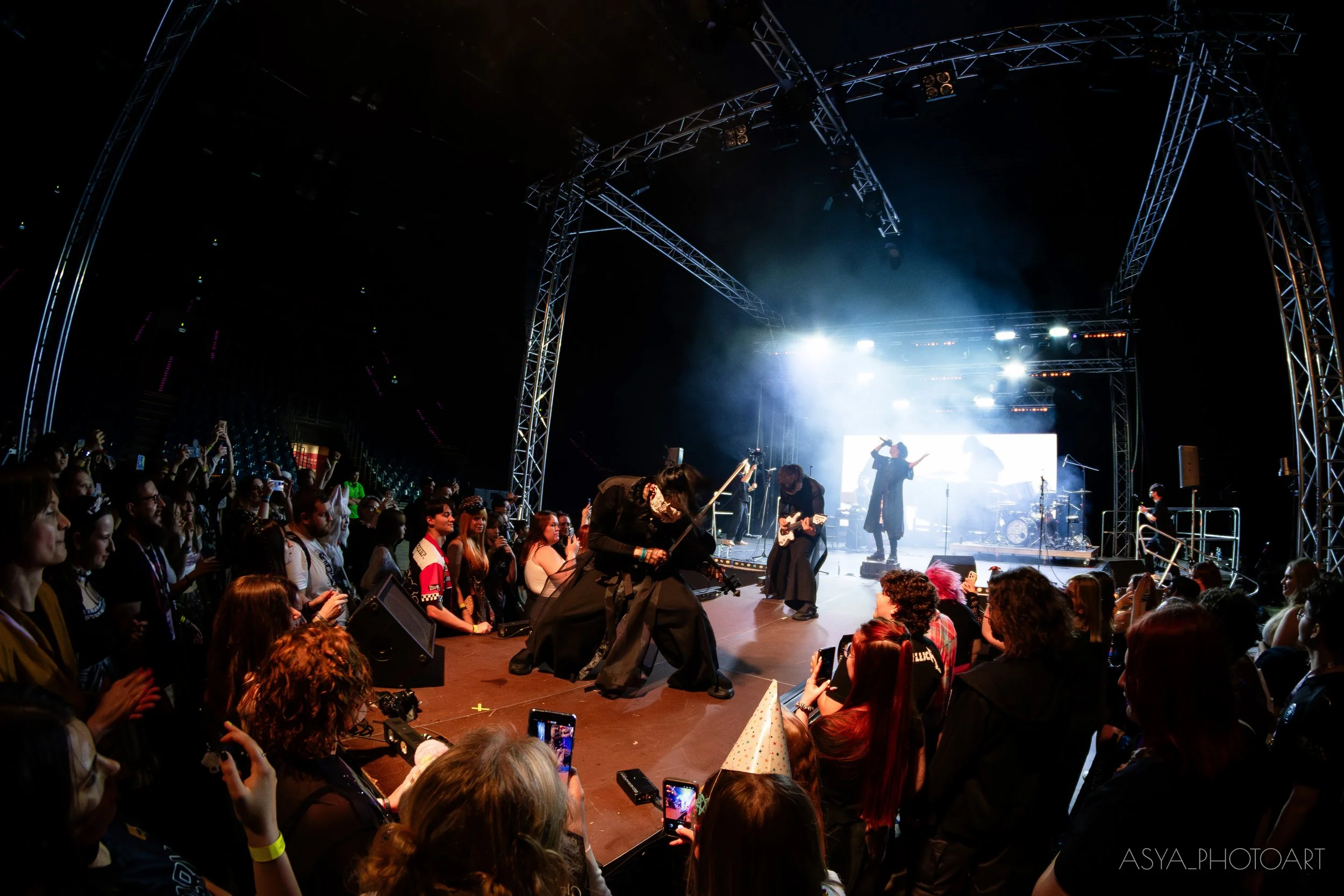 A crowd of people attending a concert or live music performance on a stage with bright lights and musical instruments.