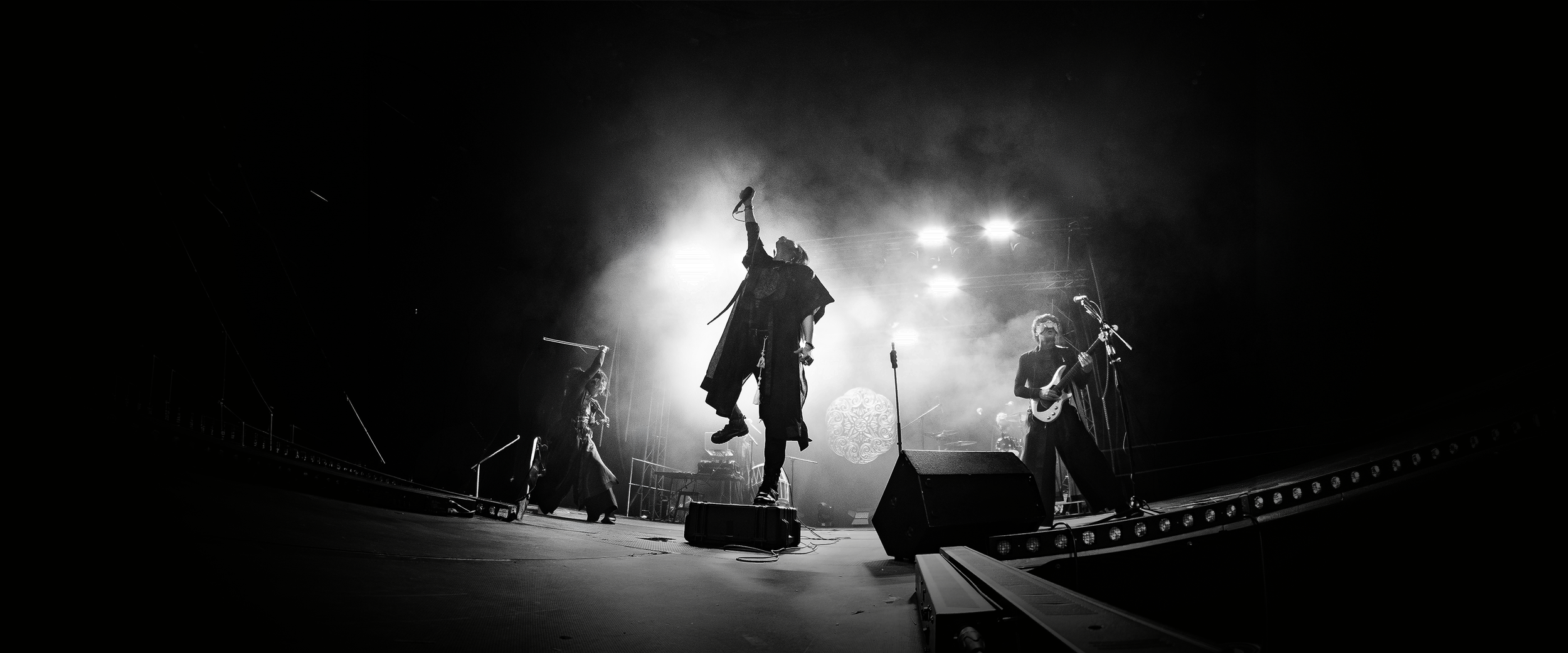 A live band performs on stage with dramatic lighting, featuring a lead singer jumping with a microphone and a guitarist playing.