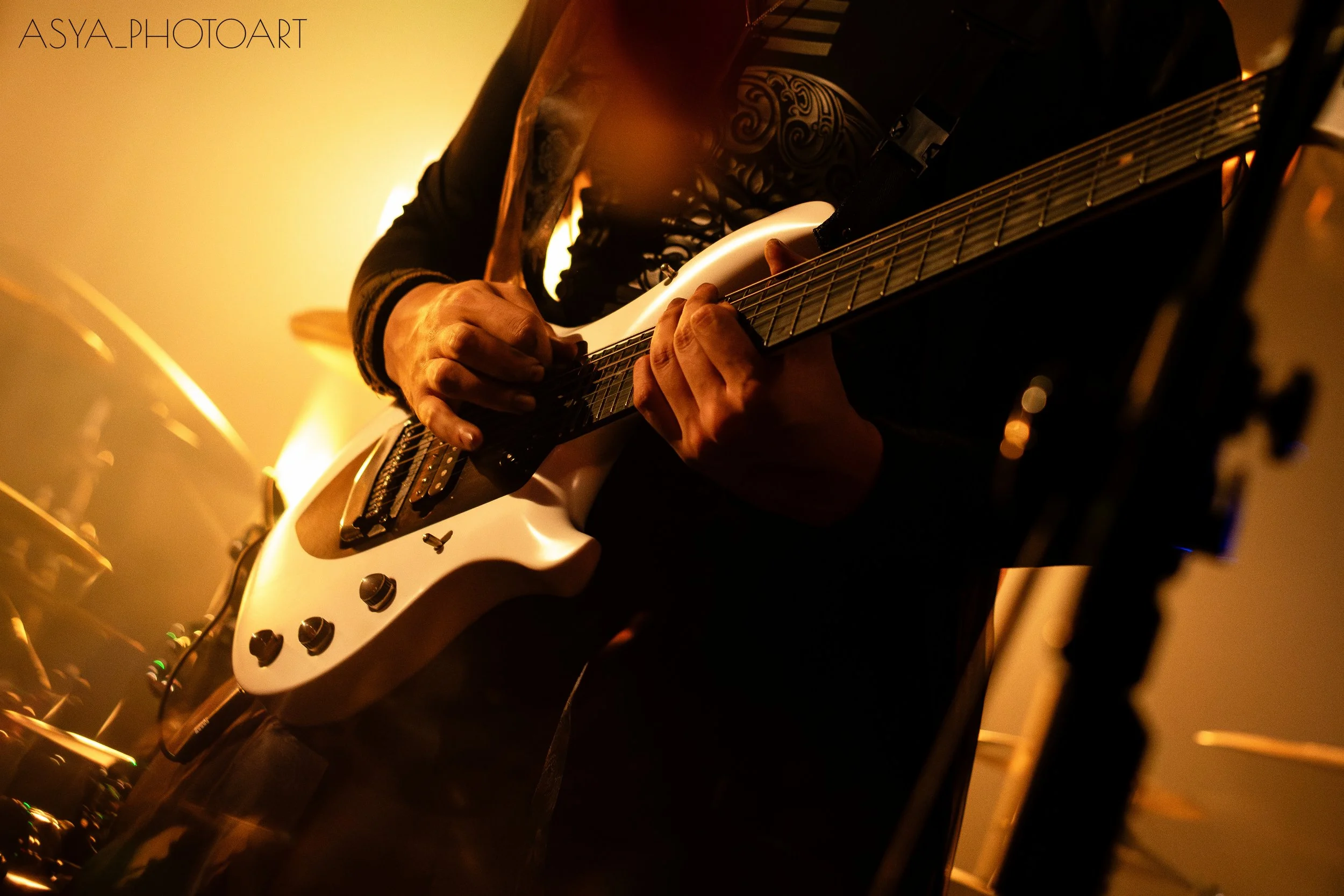 Close-up of a person playing an electric guitar with a sunburst finish, focusing on their hands and part of the guitar neck, in a warm, dimly lit setting.