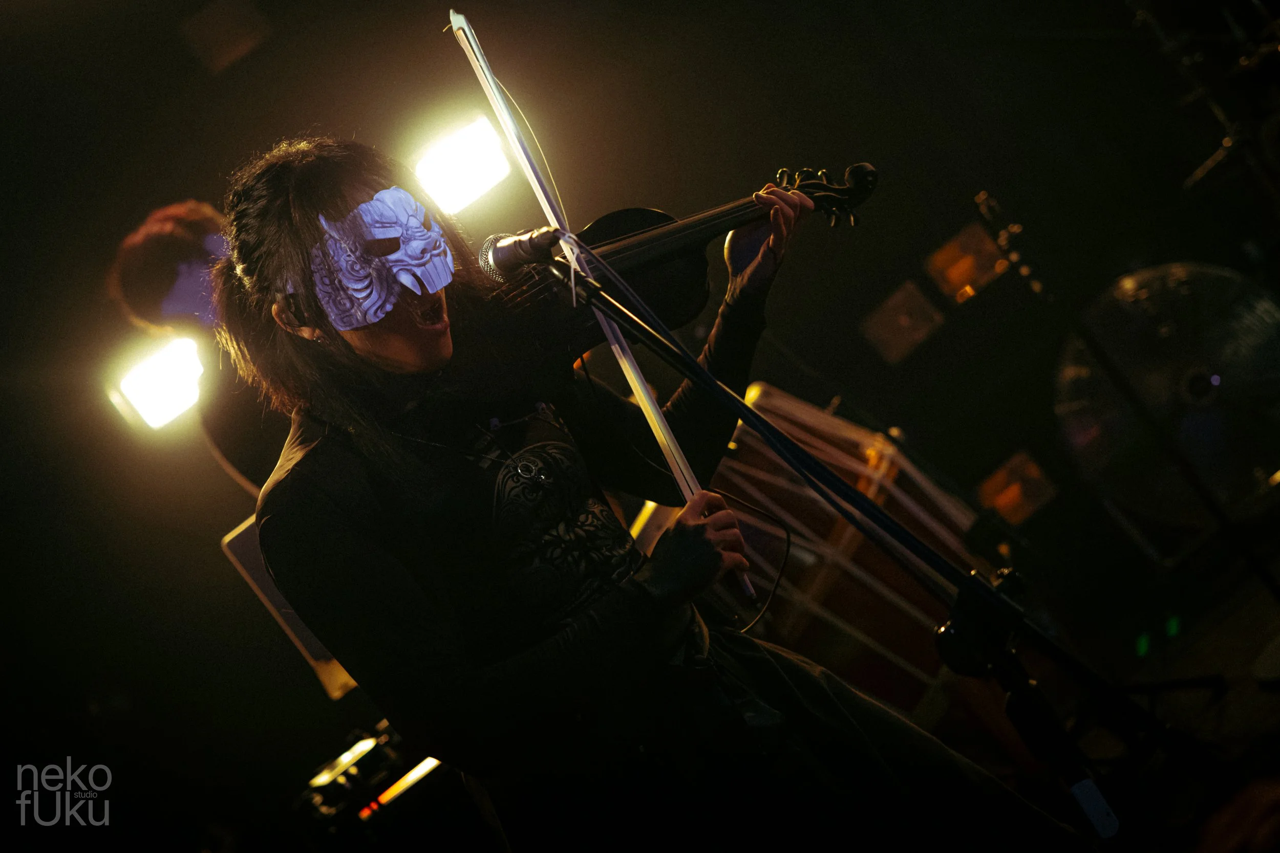 Person playing an electric violin on stage at night with bright stage lights behind them.