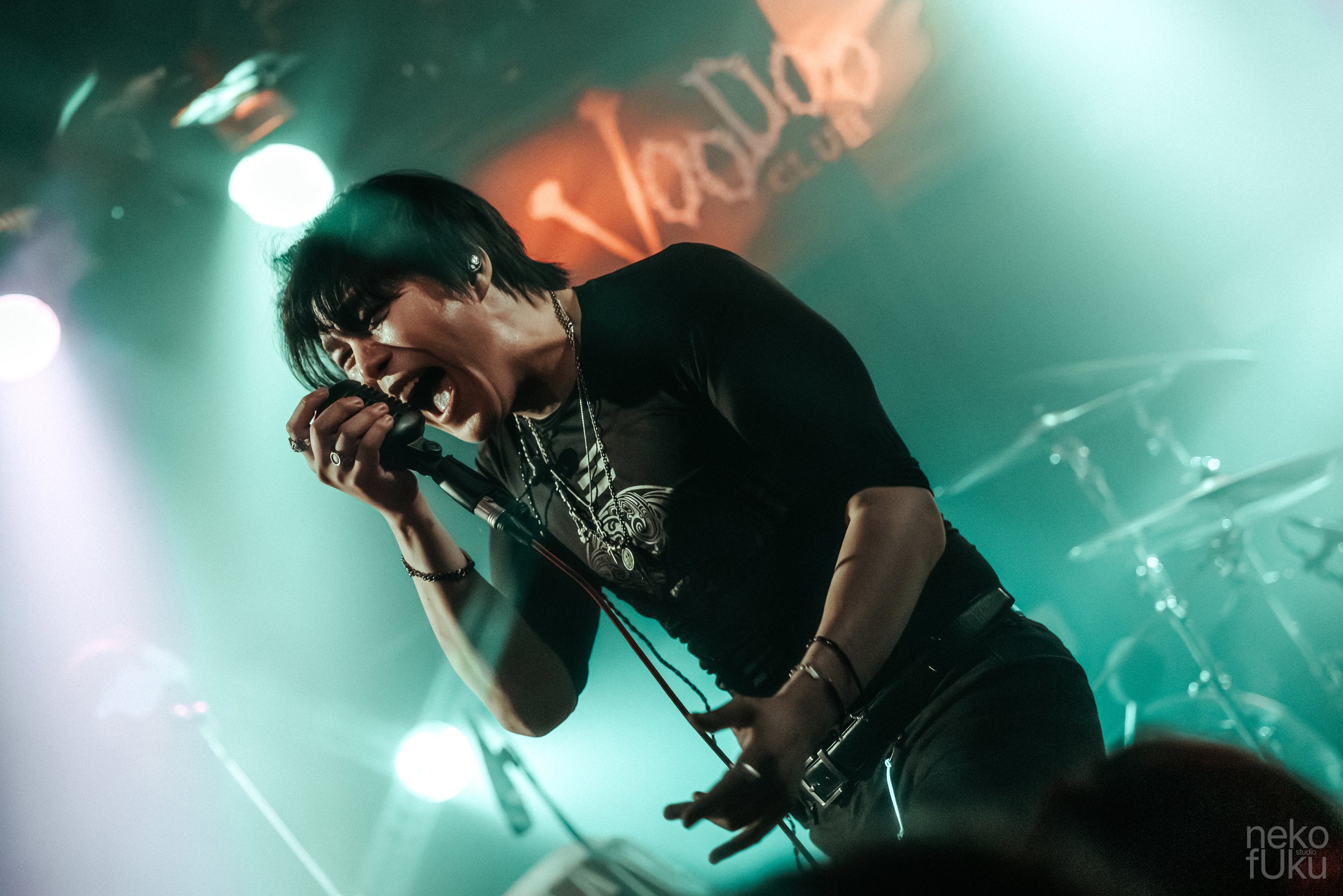 A singer passionately performs on stage, holding a microphone, with a vibrant, colorful background featuring stage lights and signage.