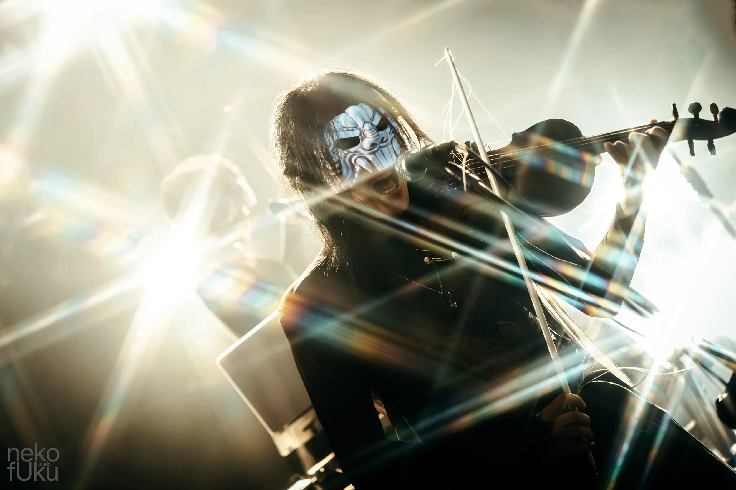 A person wearing a mask playing a violin surrounded by bright lights and lens flare effects.